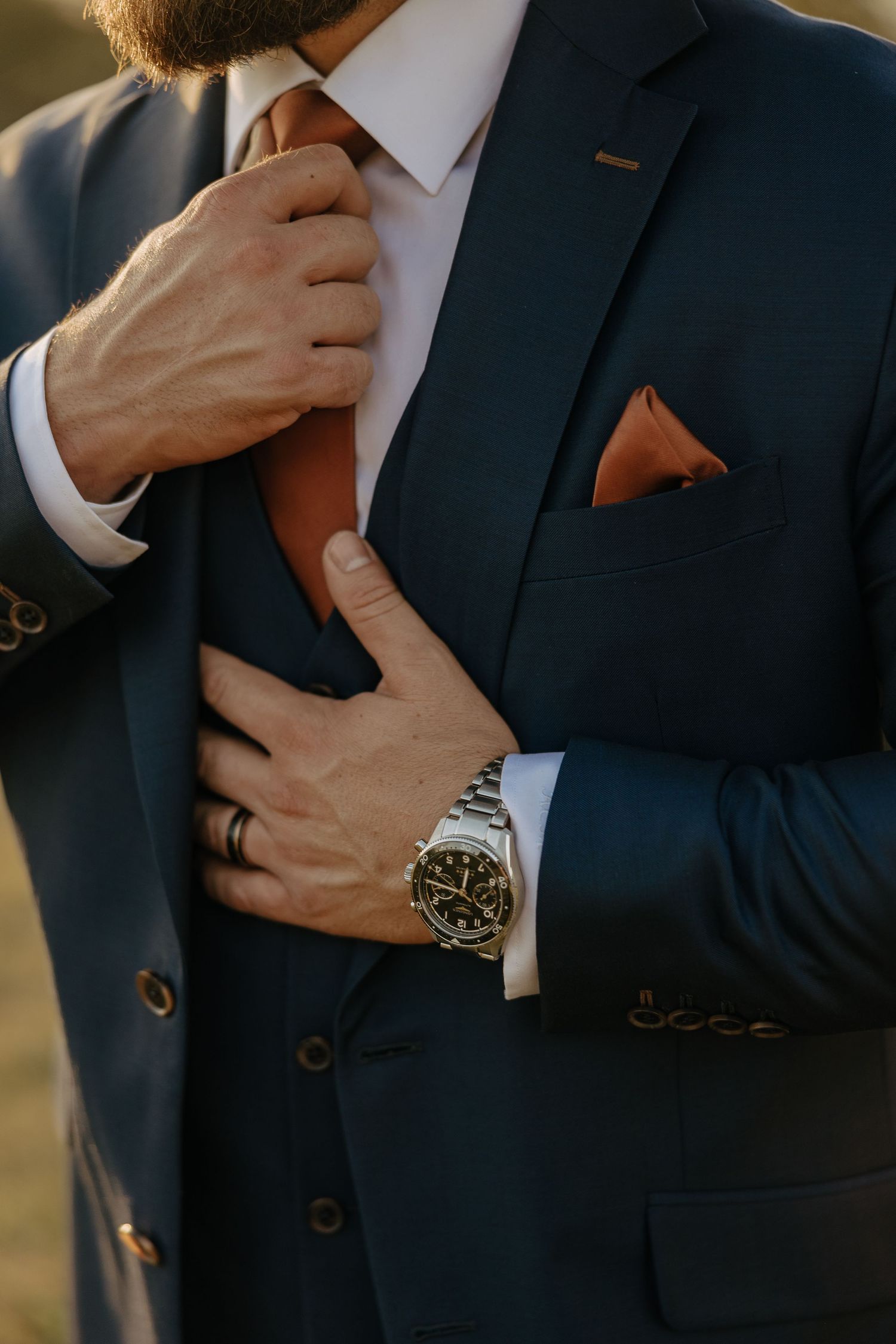 Close-up of formal attire showing navy suit jacket, tie, and luxury watch details.