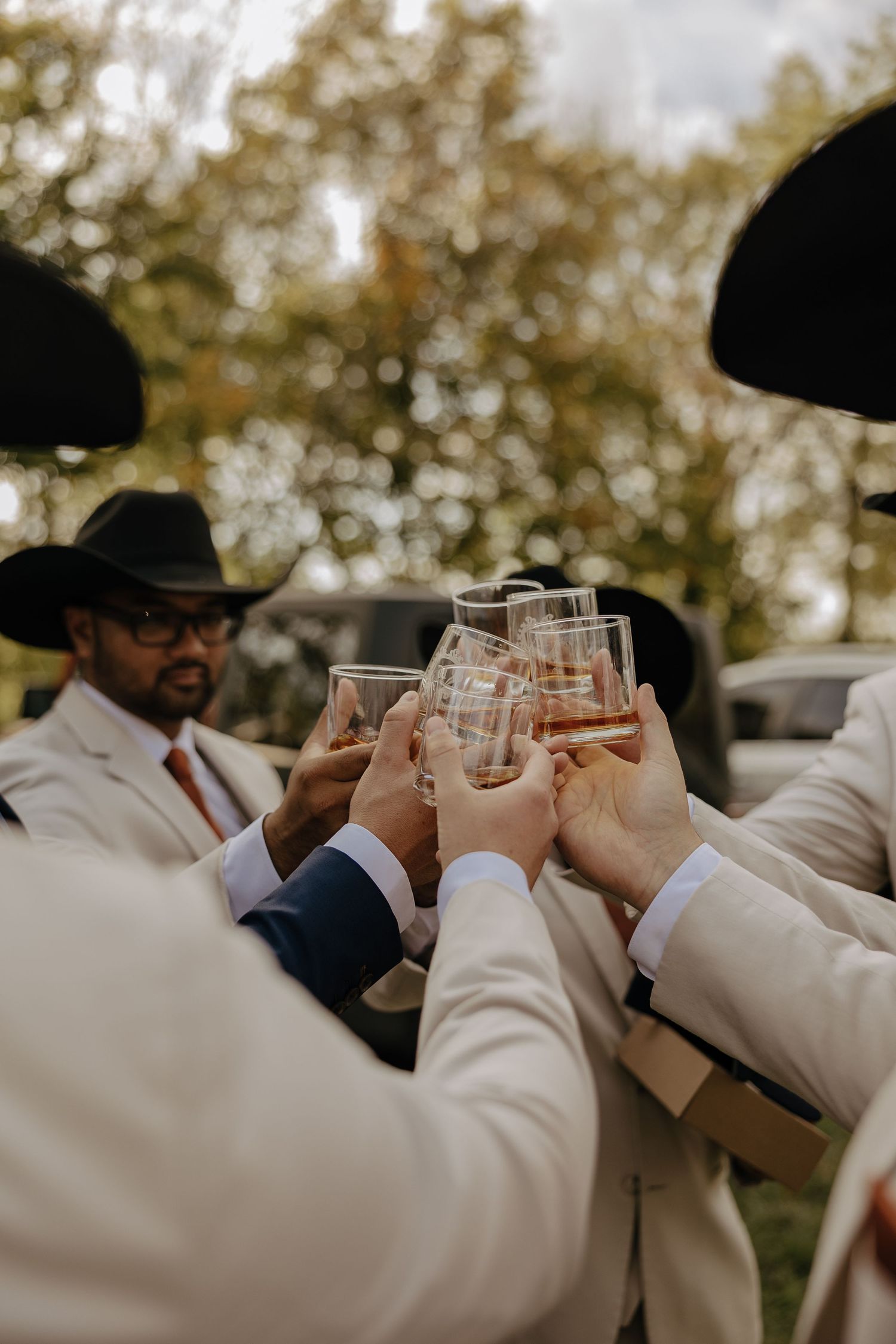 Groomsmen in cowboy hats toasting with glasses during an outdoor wedding celebration.