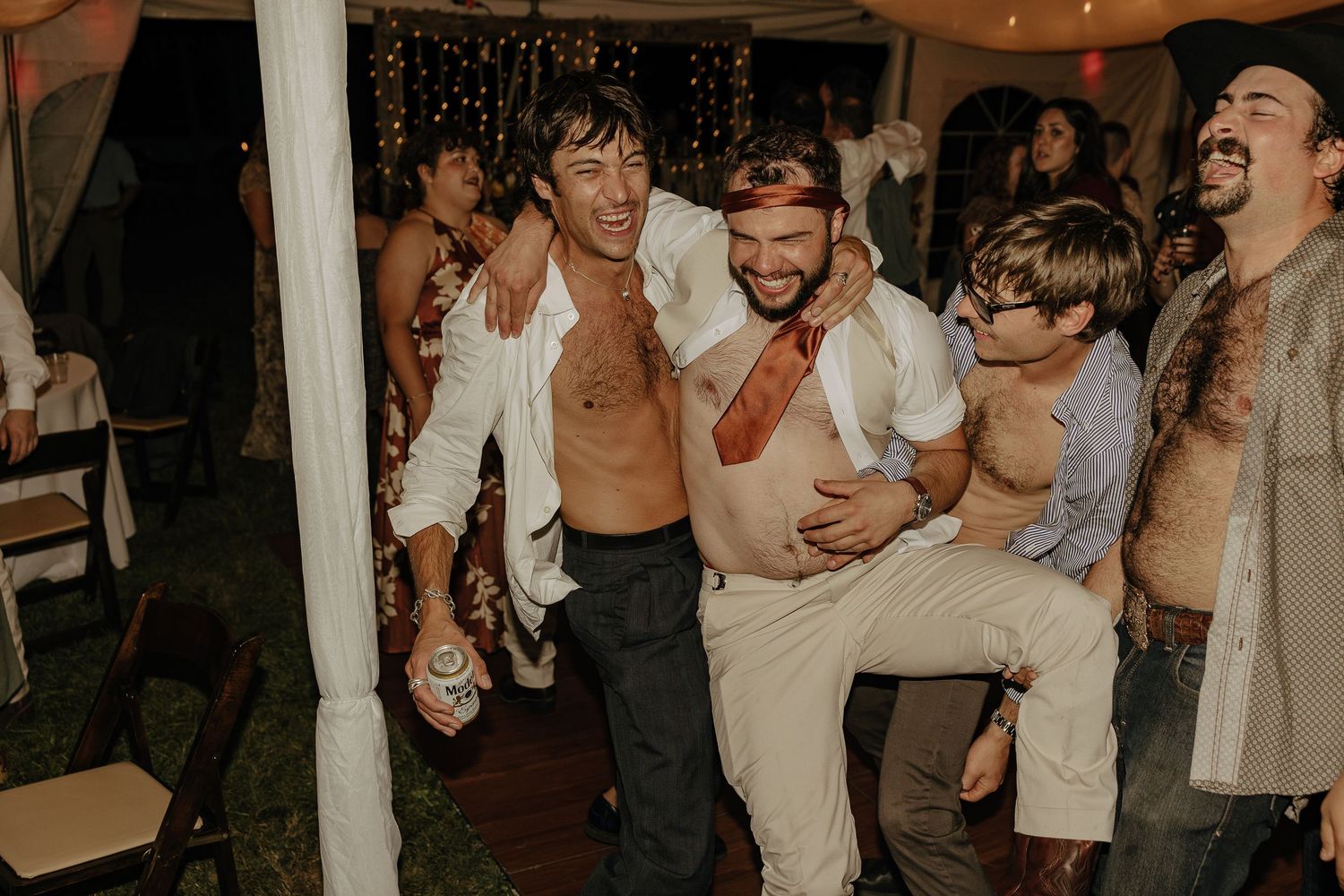Joyful wedding reception celebration with guests dancing under string lights.