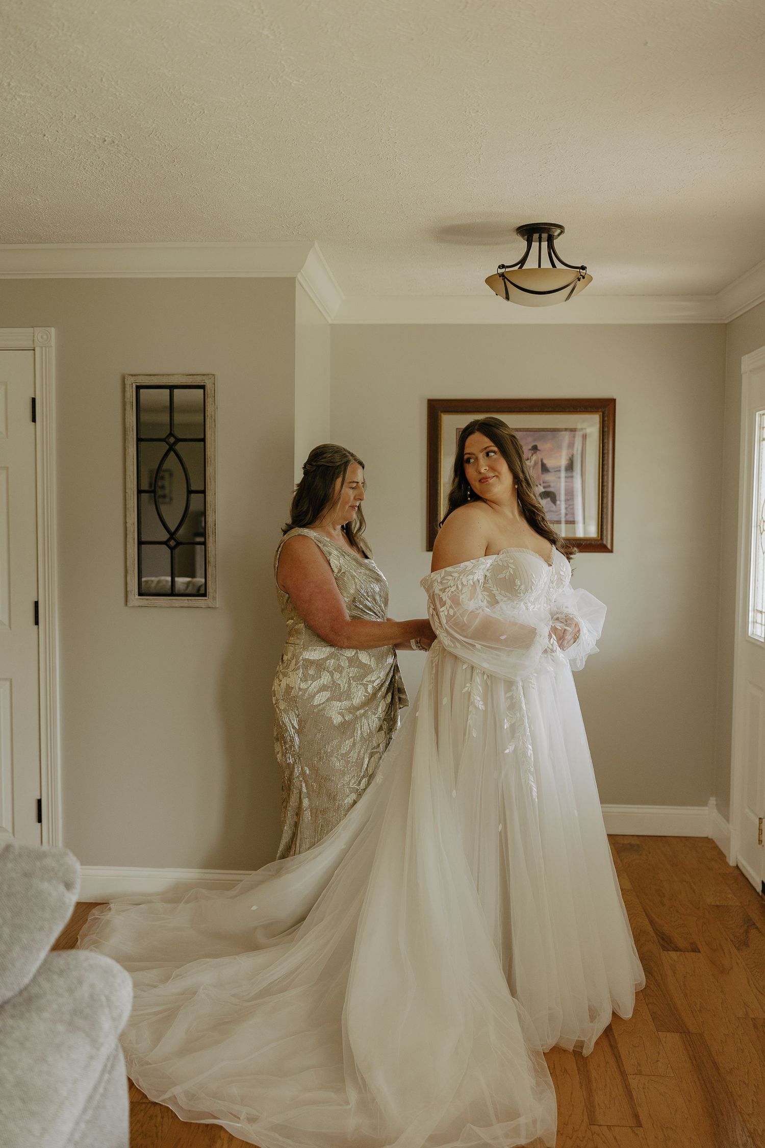 Wedding dress preparation scene showing flowing white gown with intricate lace details in a sunlit room.