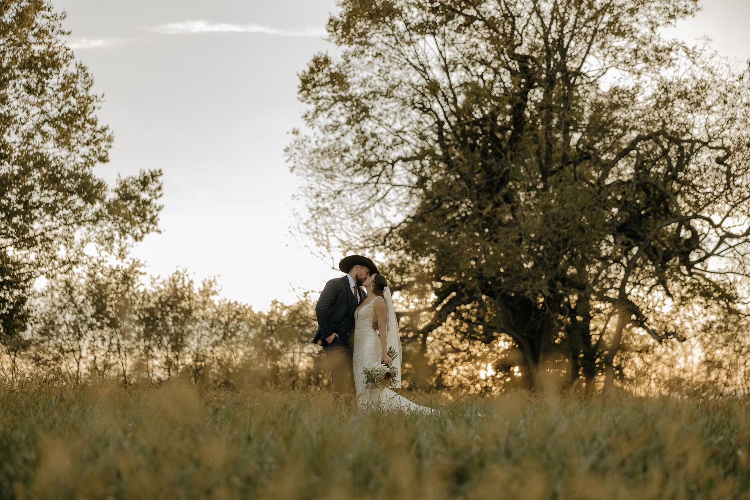 Silhouettes of a couple walking through a field at sunset during their wedding.