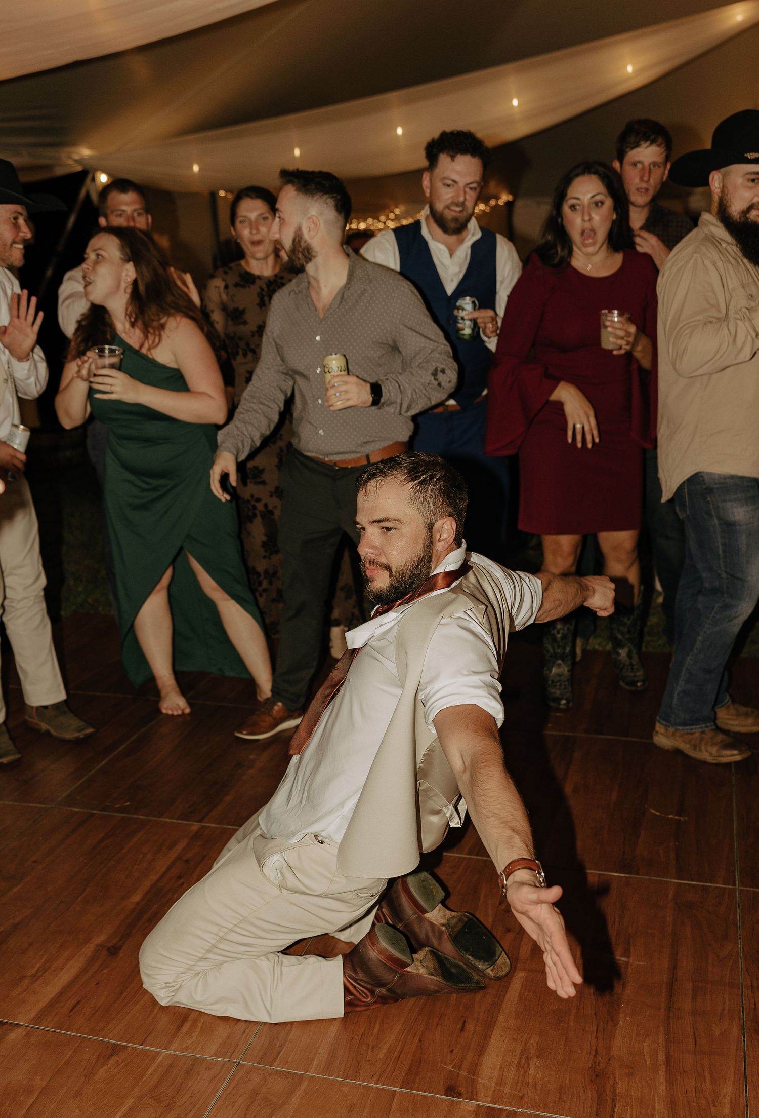 Wedding guests performing energetic dance moves on a wooden dance floor at the reception.