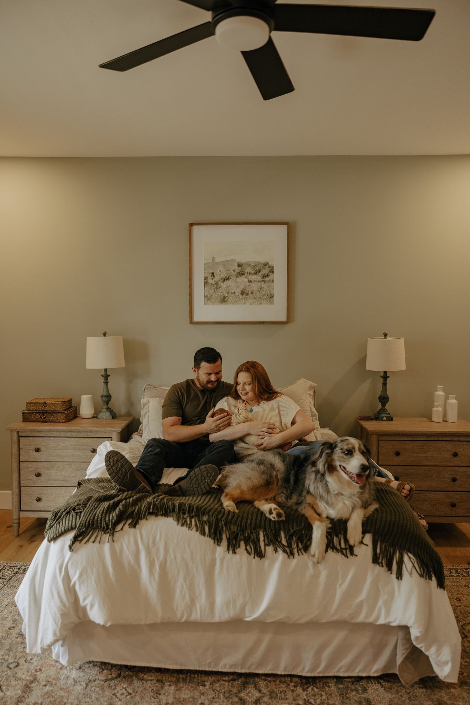Family relaxes on white bed with their dog while sharing intimate moments.