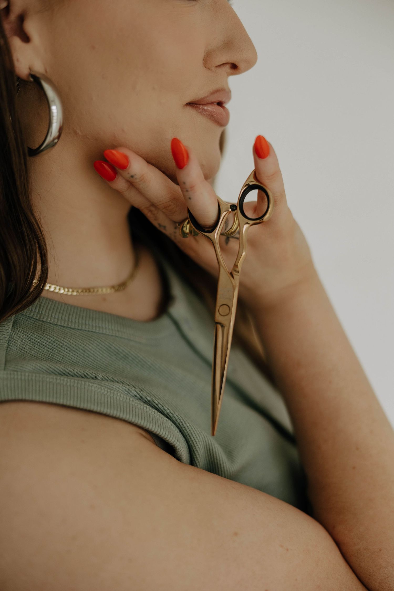 Close-up of gold scissors held against sage green fabric with red manicured nails.