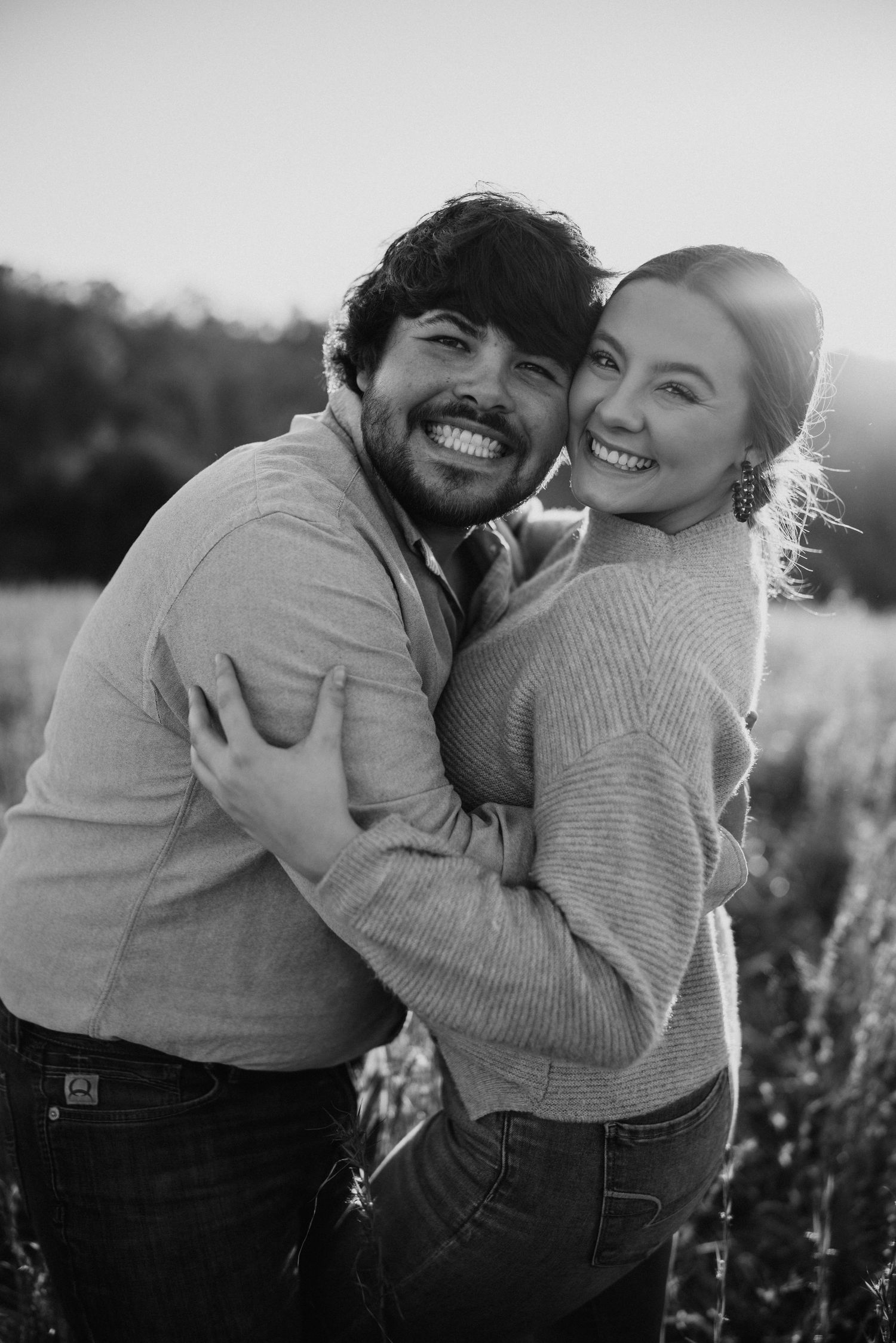 Couple laughing and embracing during black and white countryside photoshoot at sunset.