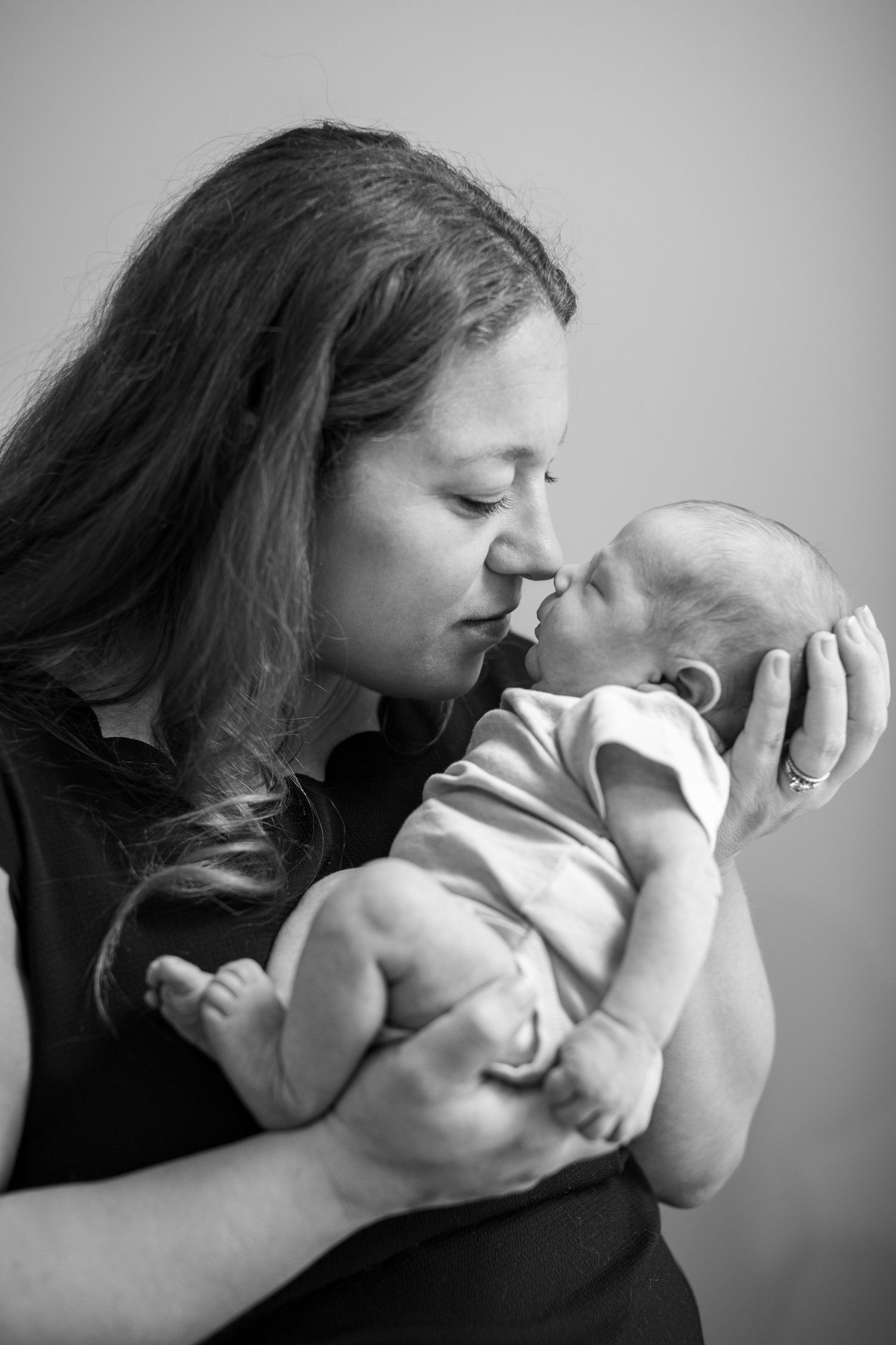 Black and white photo of a mother tenderly touching noses with her newborn baby while cradling it in her arms.