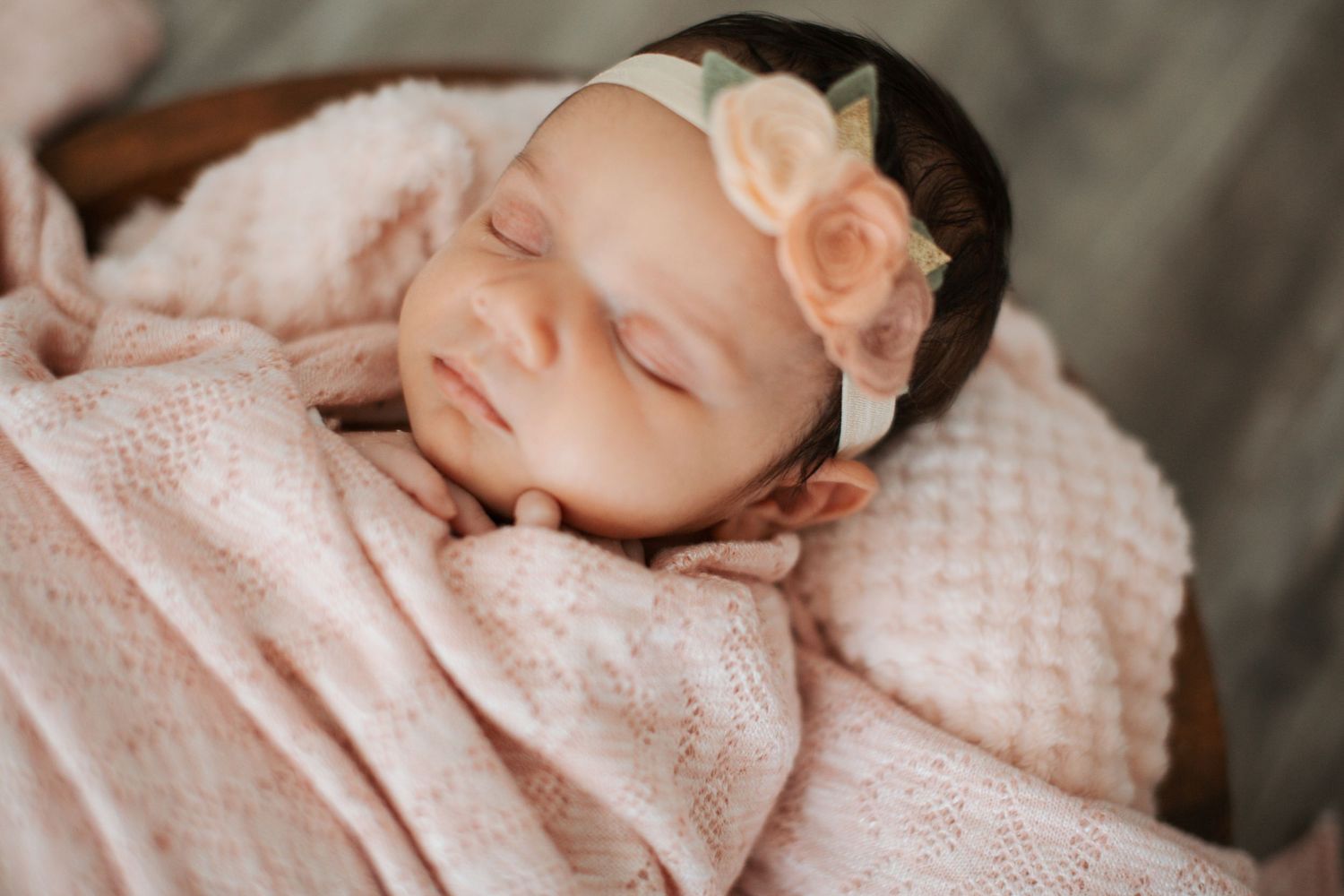Sleeping newborn wrapped in textured pink blanket against white background.