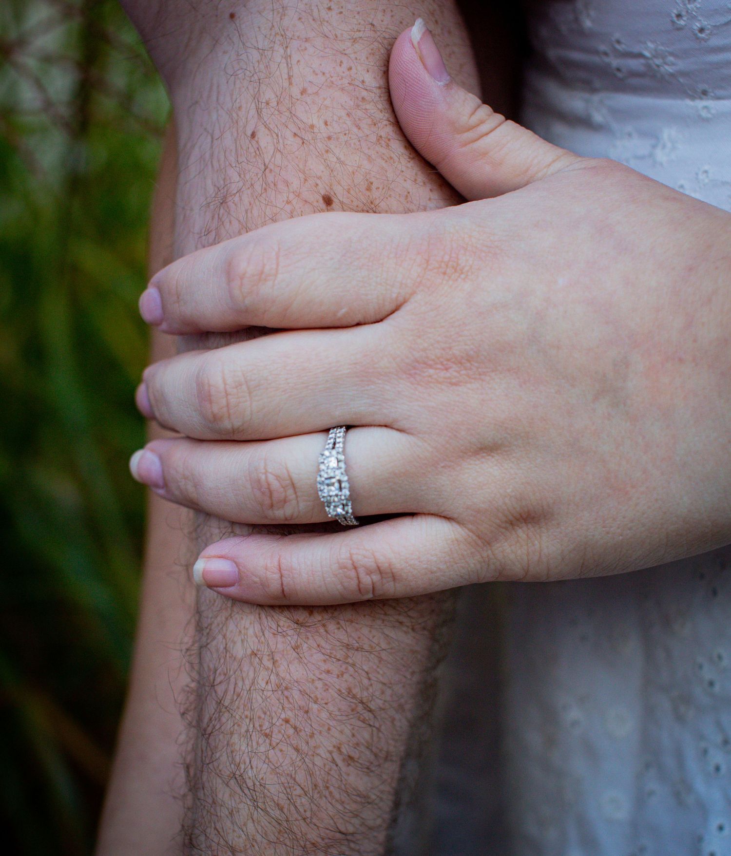 Close-up of hands with an engagement ring embracing in an outdoor setting.