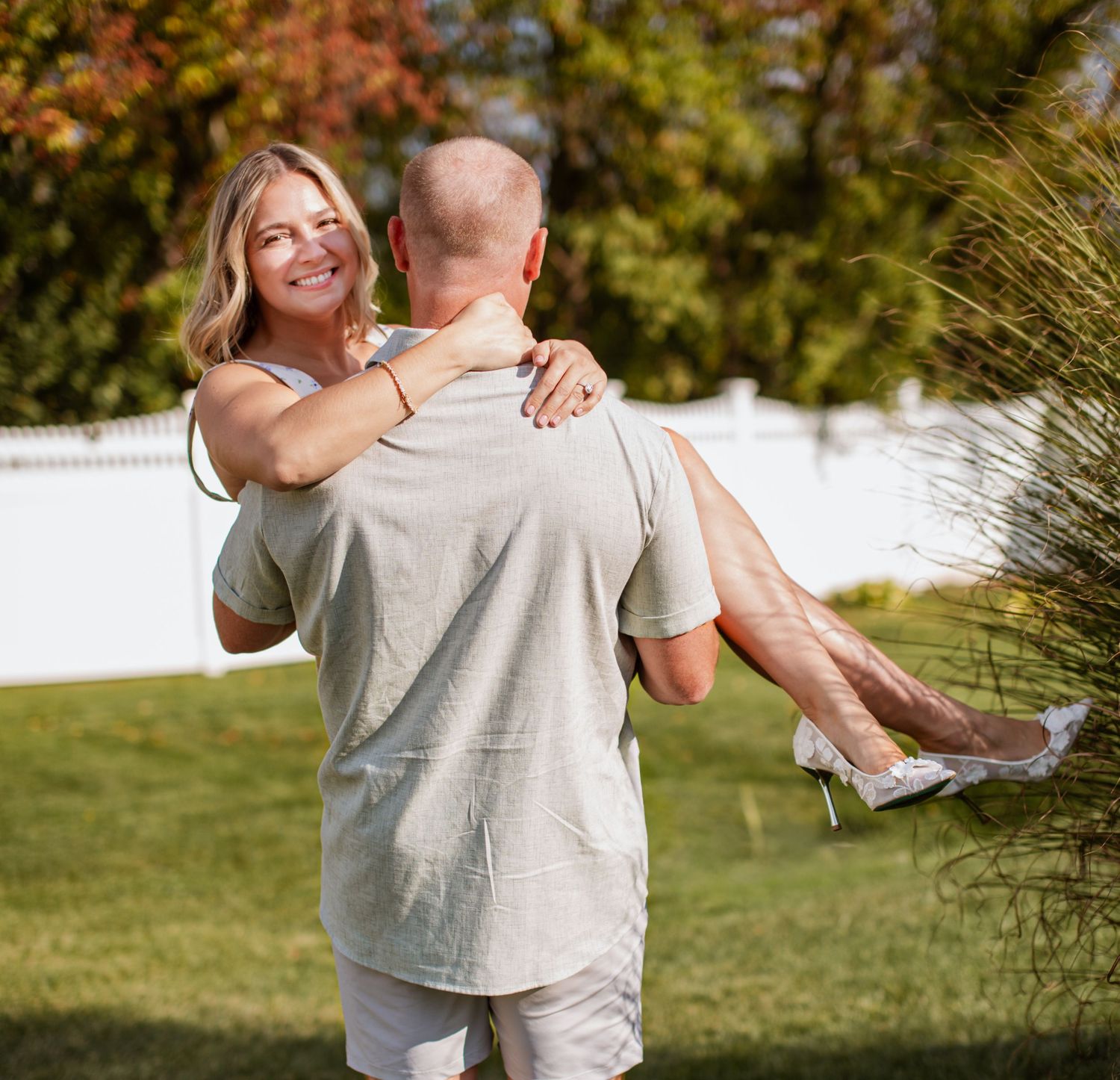 A couple embraces in a sunny outdoor setting with green grass in the background.