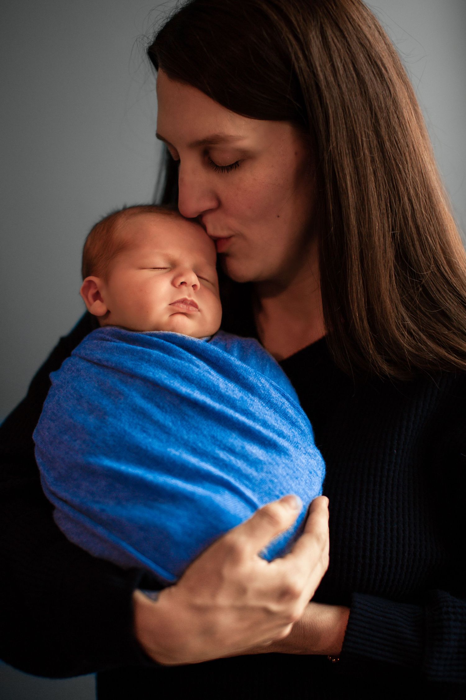 A tender moment captured in black and white as a parent cradles and kisses a sleeping baby wrapped in blue blanket.