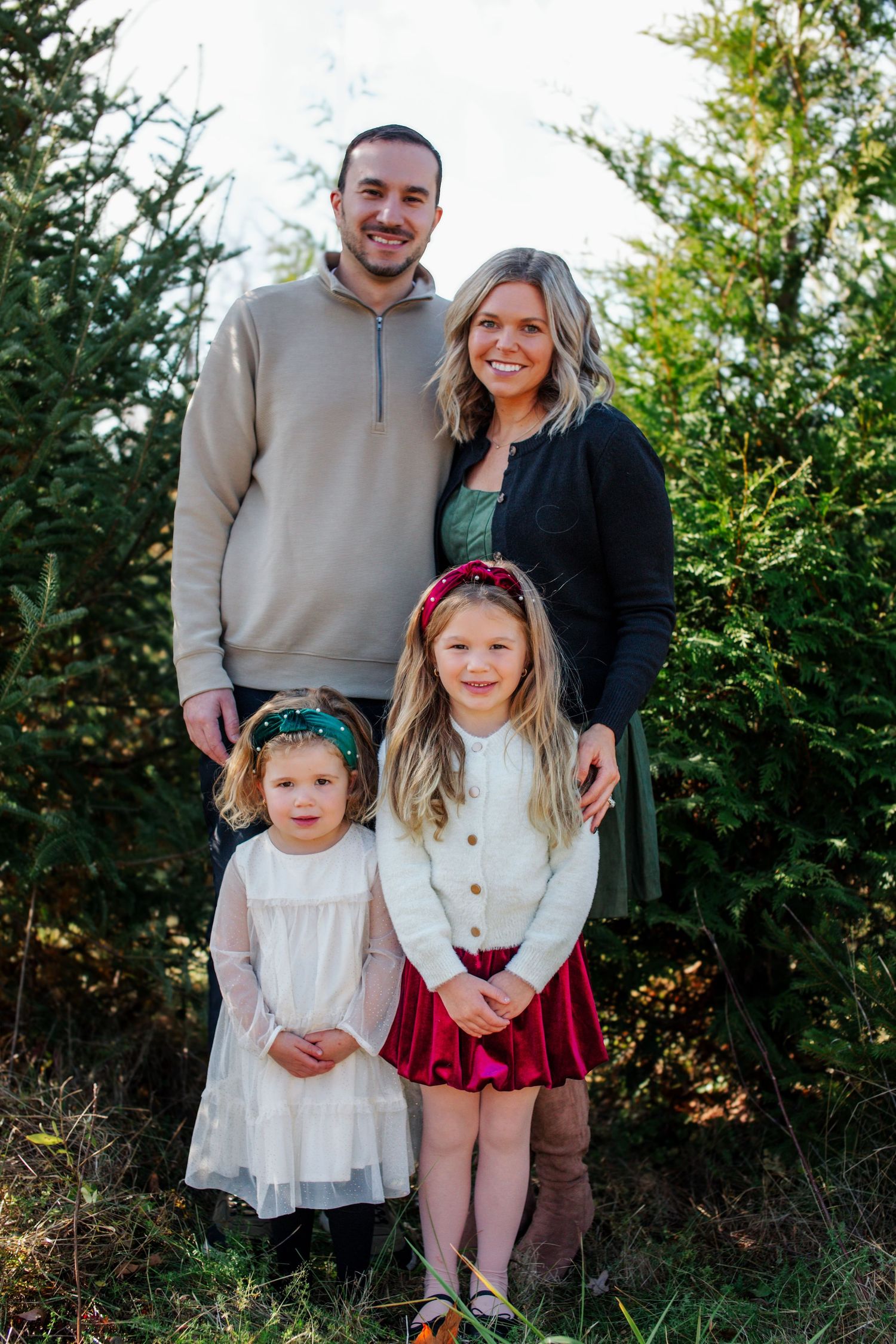 A family poses together outdoors against a backdrop of evergreen trees during a sunny photo session.