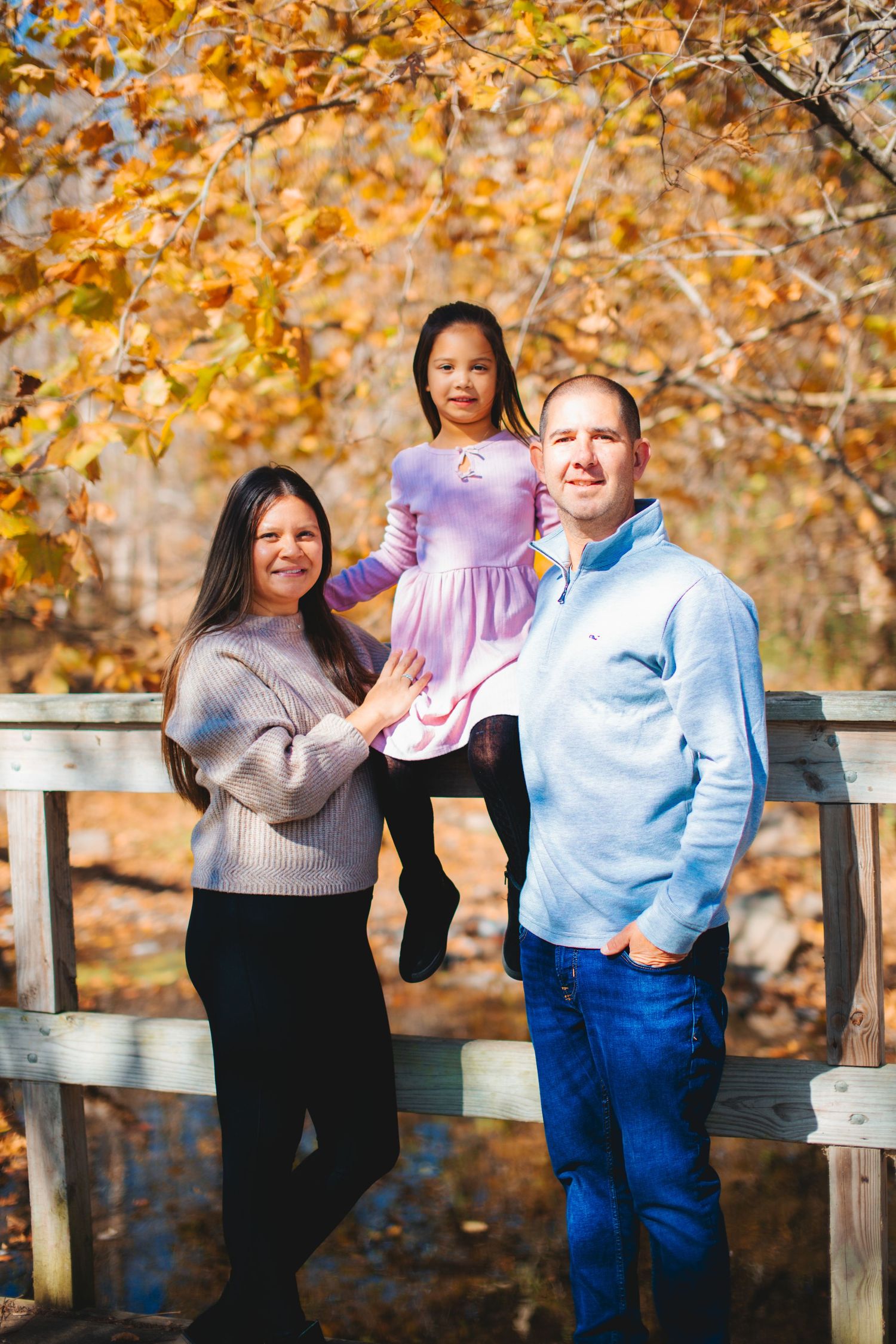 A family poses on a wooden deck surrounded by vibrant autumn foliage.
