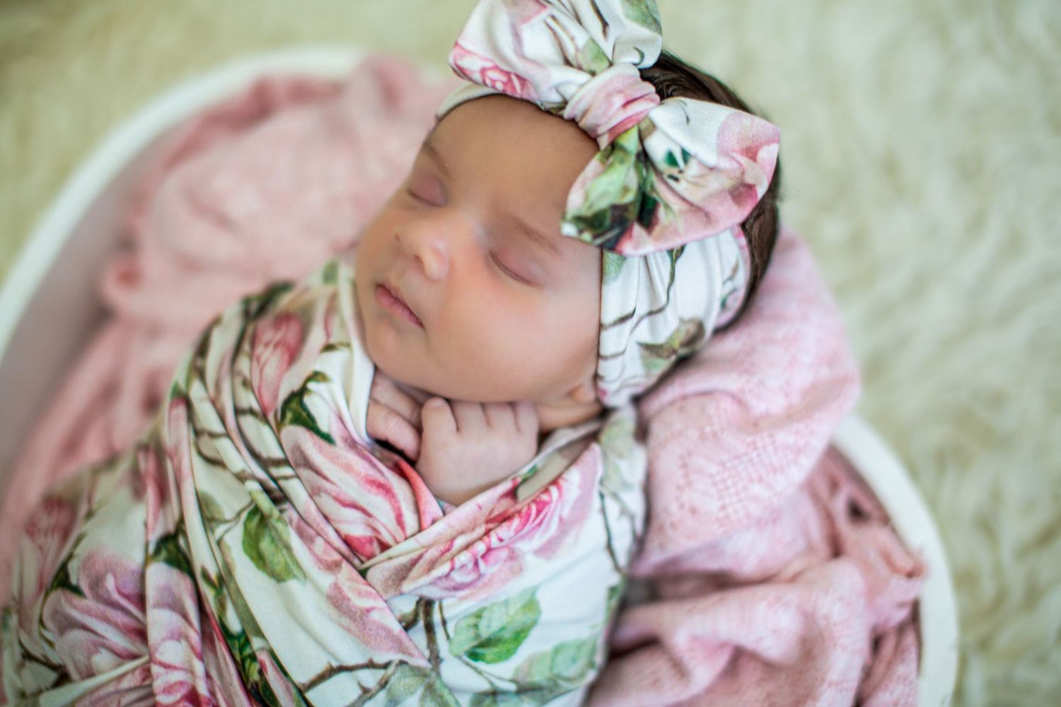 Artistic newborn portrait with floral accessories and pink swaddle wrap.