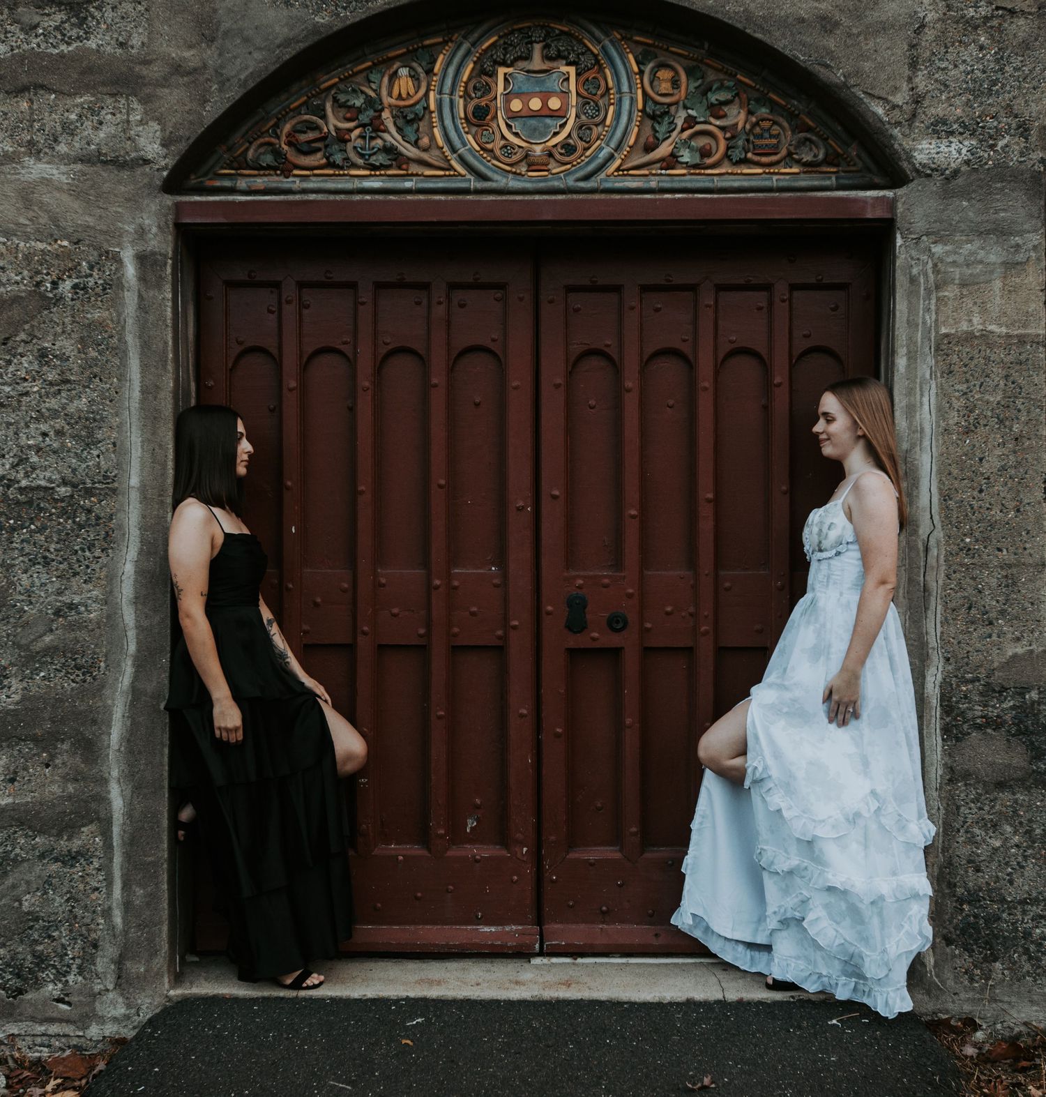 Two people in contrasting black and blue dresses pose in front of an ornate red door.