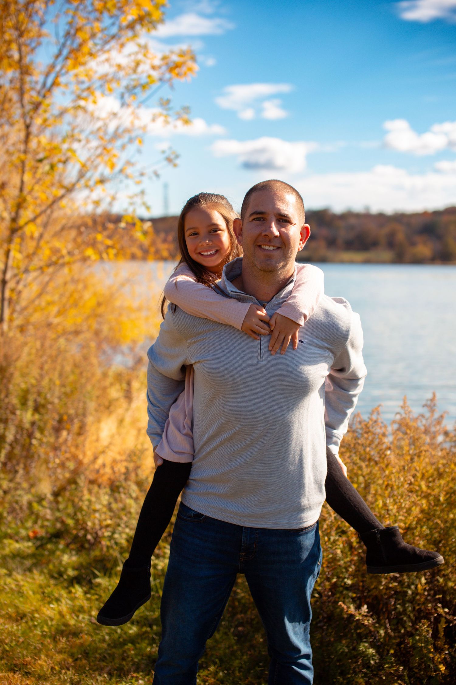 A piggyback ride moment captured against a scenic fall lake backdrop with yellow trees.