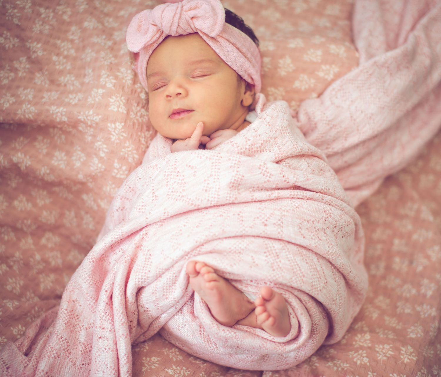 Newborn photography with soft pink wrap and delicate lace details.