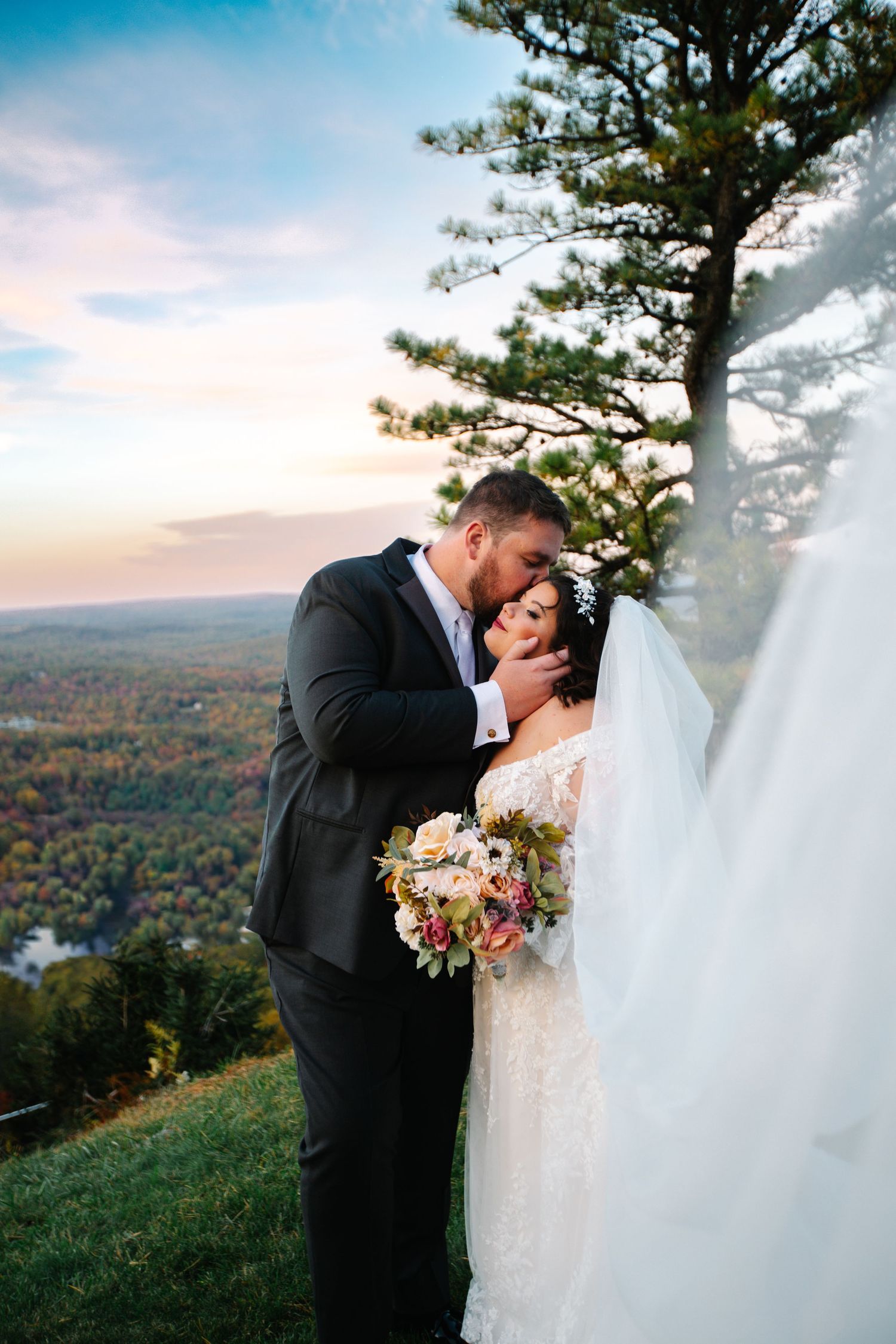 Intimate wedding portrait of couple embracing on mountaintop during sunset.