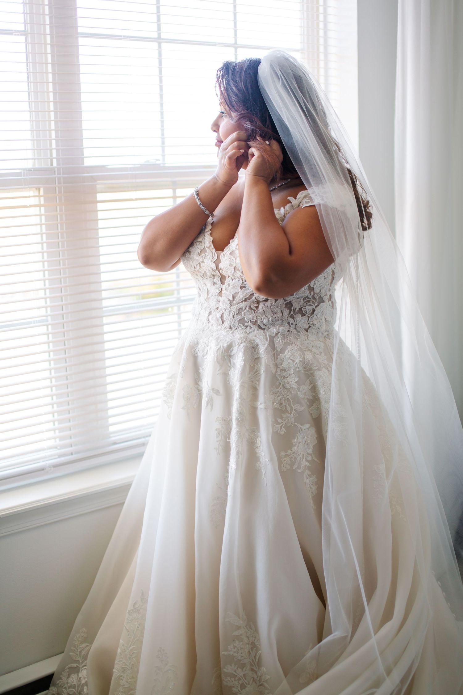 A bride in a flowing white lace wedding gown and veil stands by a window in a sequence of candid moments.
