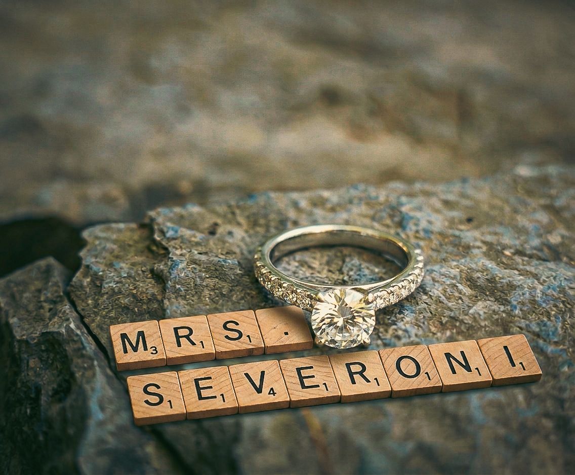 Diamond engagement ring on rock beside Scrabble tiles spelling MRS. SEVERONI, a romantic marriage proposal keepsake photo.