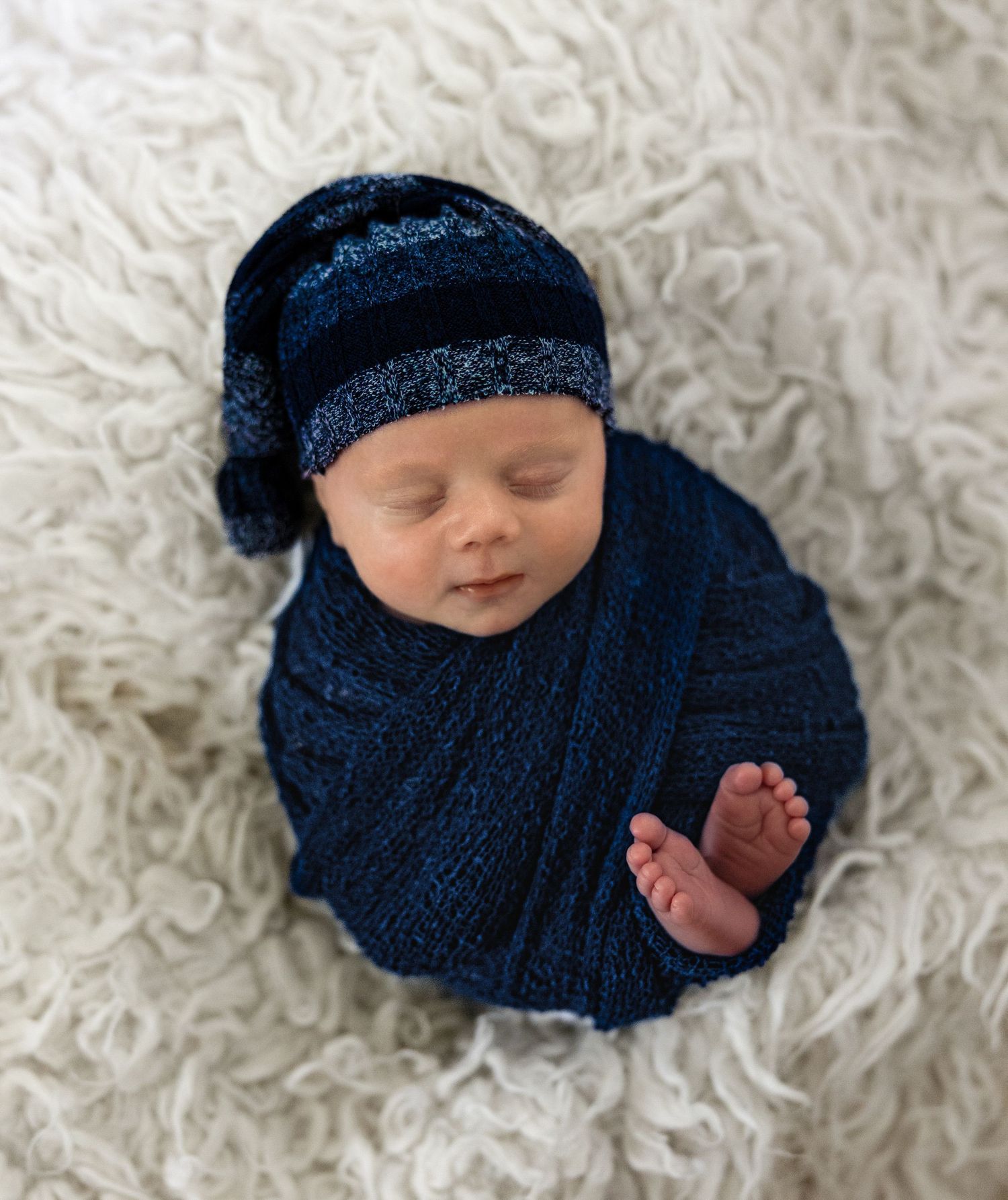 Newborn wearing navy knit wrap on white textured rug.