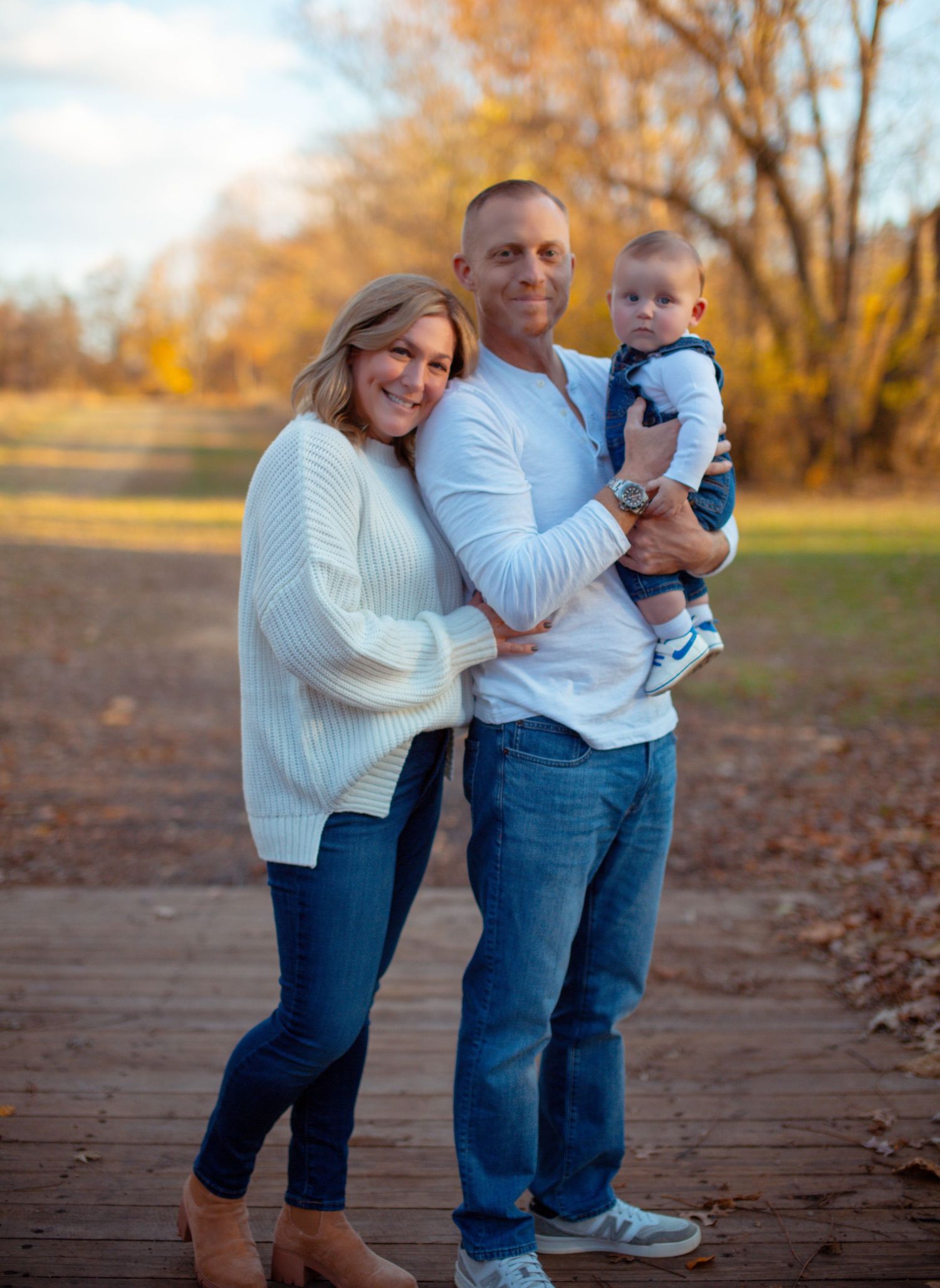 A family portrait on a wooden path surrounded by fall trees and golden light.
