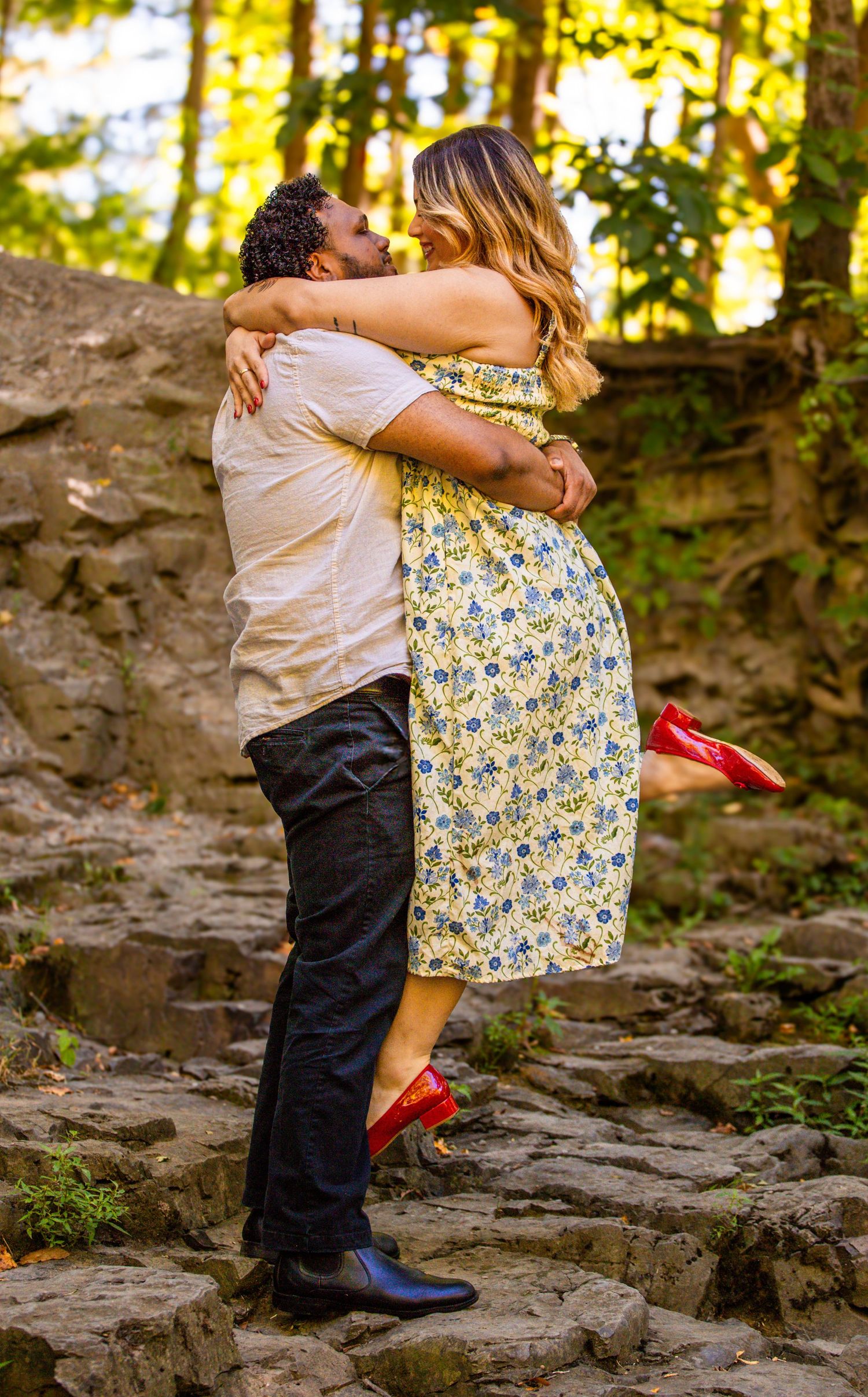 Romantic couple embracing on stone steps in a sunlit forest setting.