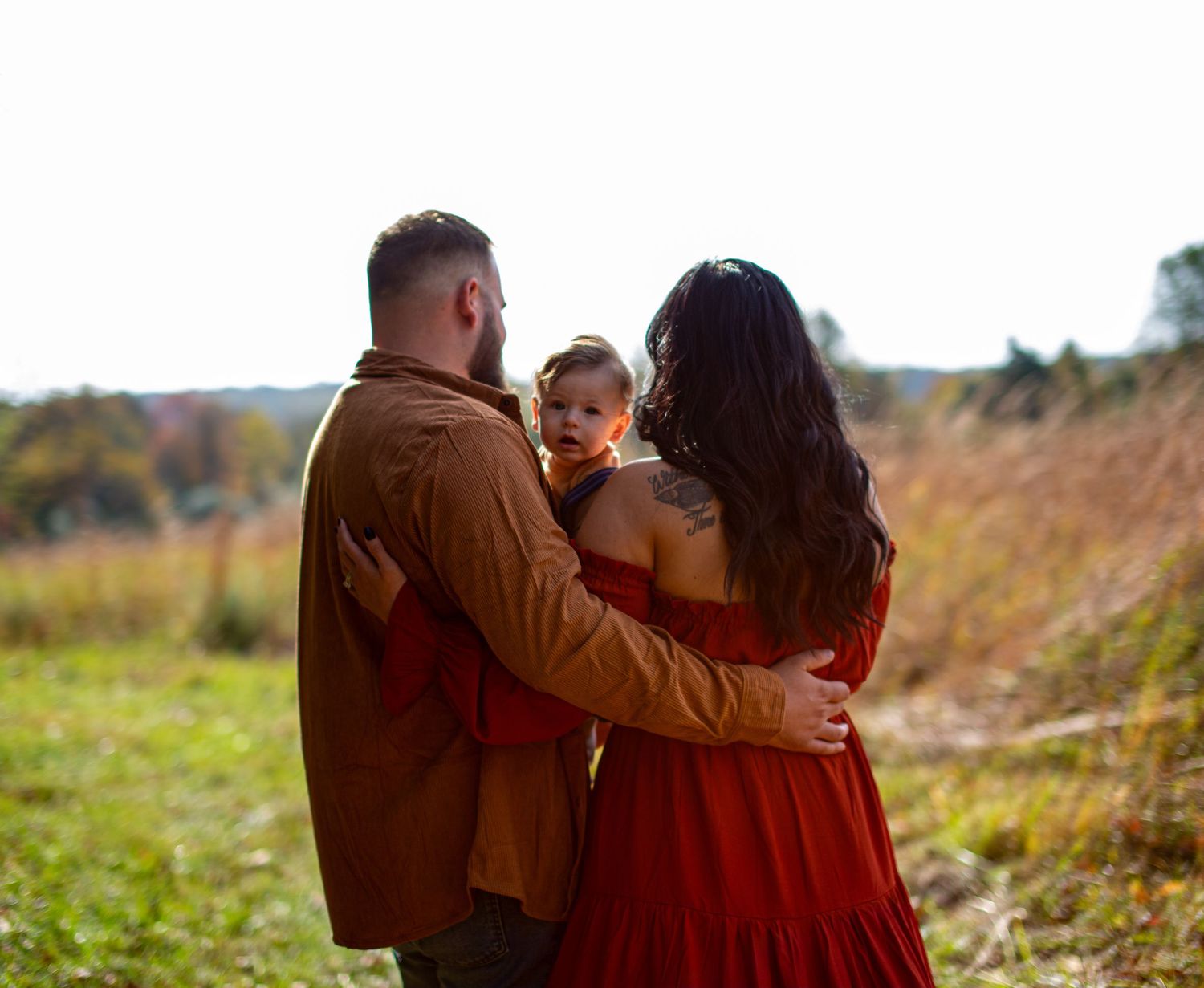 A tender family moment captured from behind against a golden autumn field.