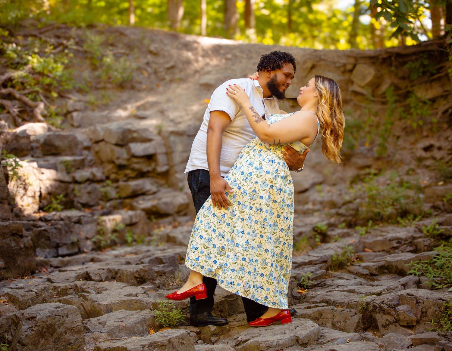A couple sits together on stone steps in a sunlit outdoor setting wearing casual summer attire.