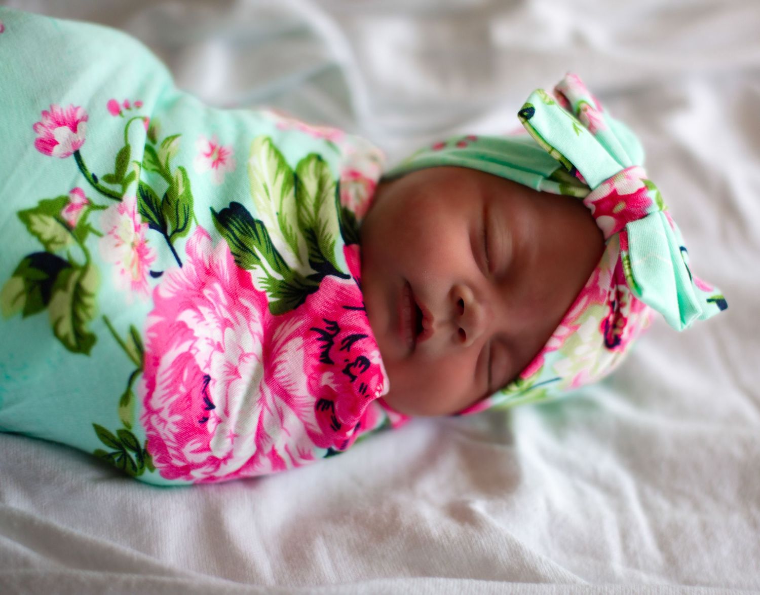 Baby resting on soft bedding with floral headband and mint green accents.