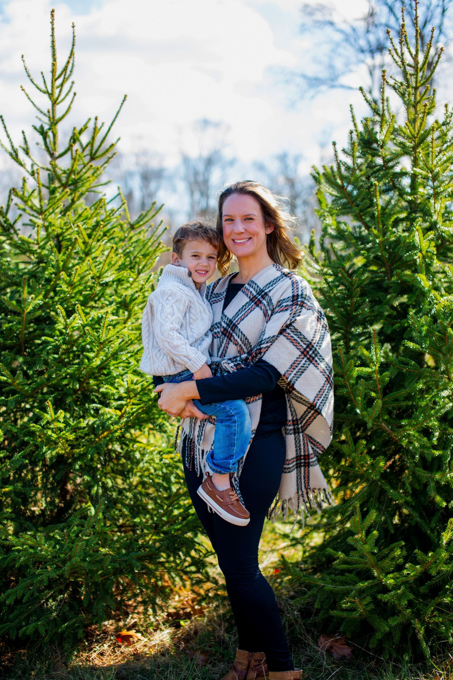 A family shares joyful moments among evergreen trees at a Christmas tree farm on a sunny winter day.