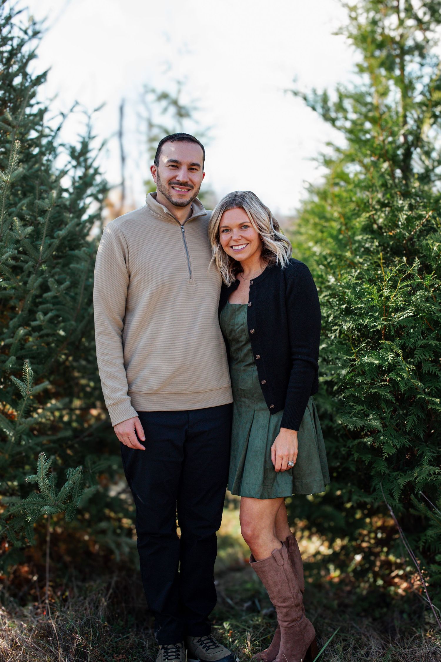A couple poses together outdoors in front of evergreen trees during a fall photo session.