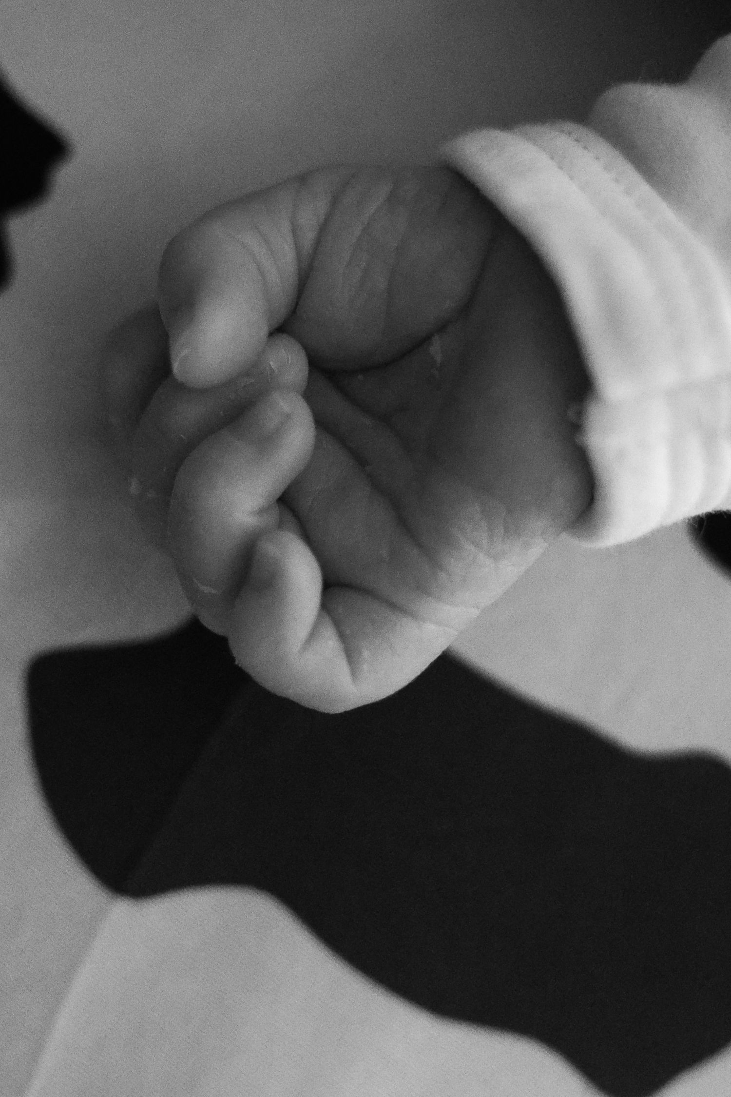 Close-up black and white photo of a newborn baby's tiny clenched fist in a white sleeve.