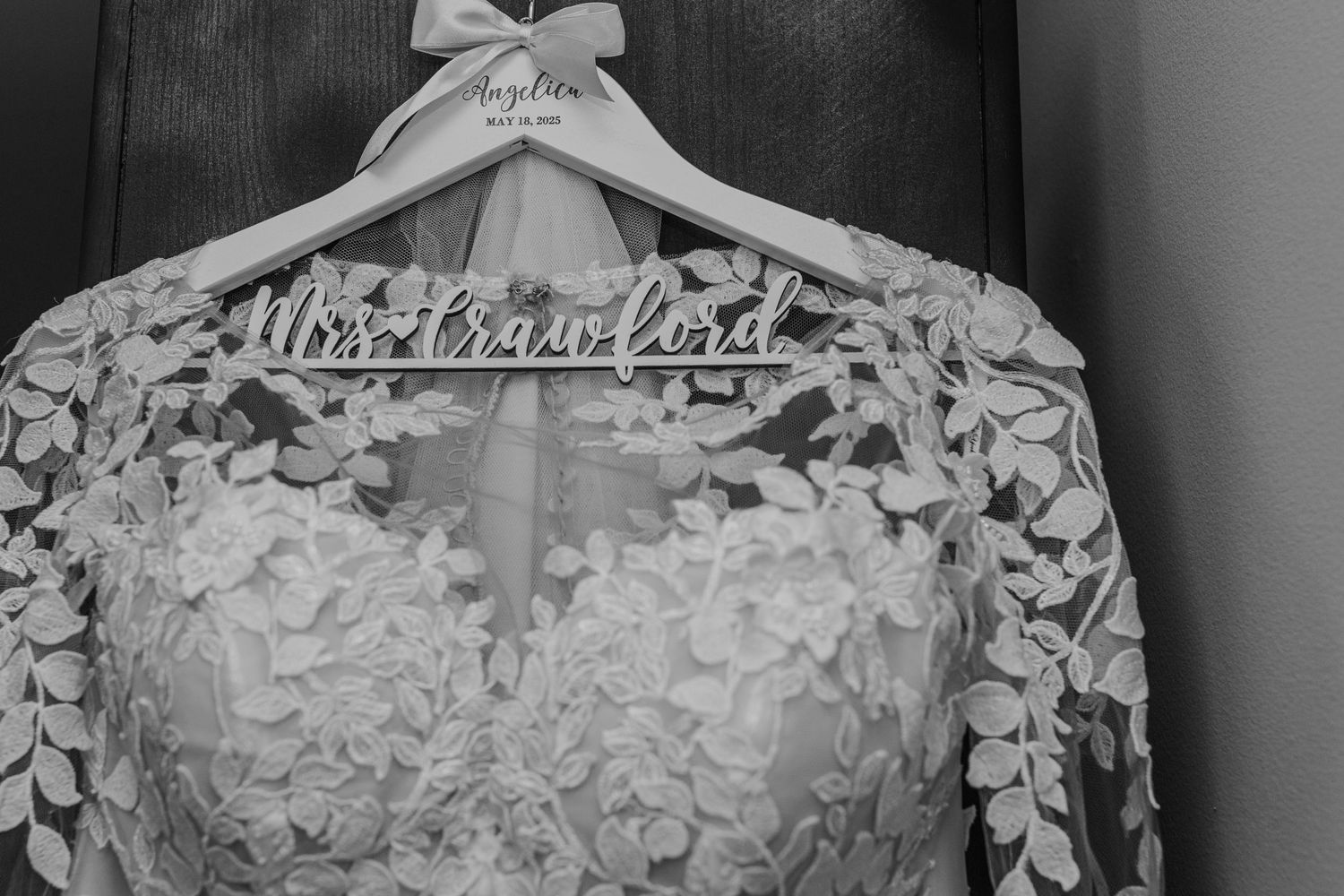 A close-up view of delicate white floral lace details on a wedding dress hanging on a hanger.