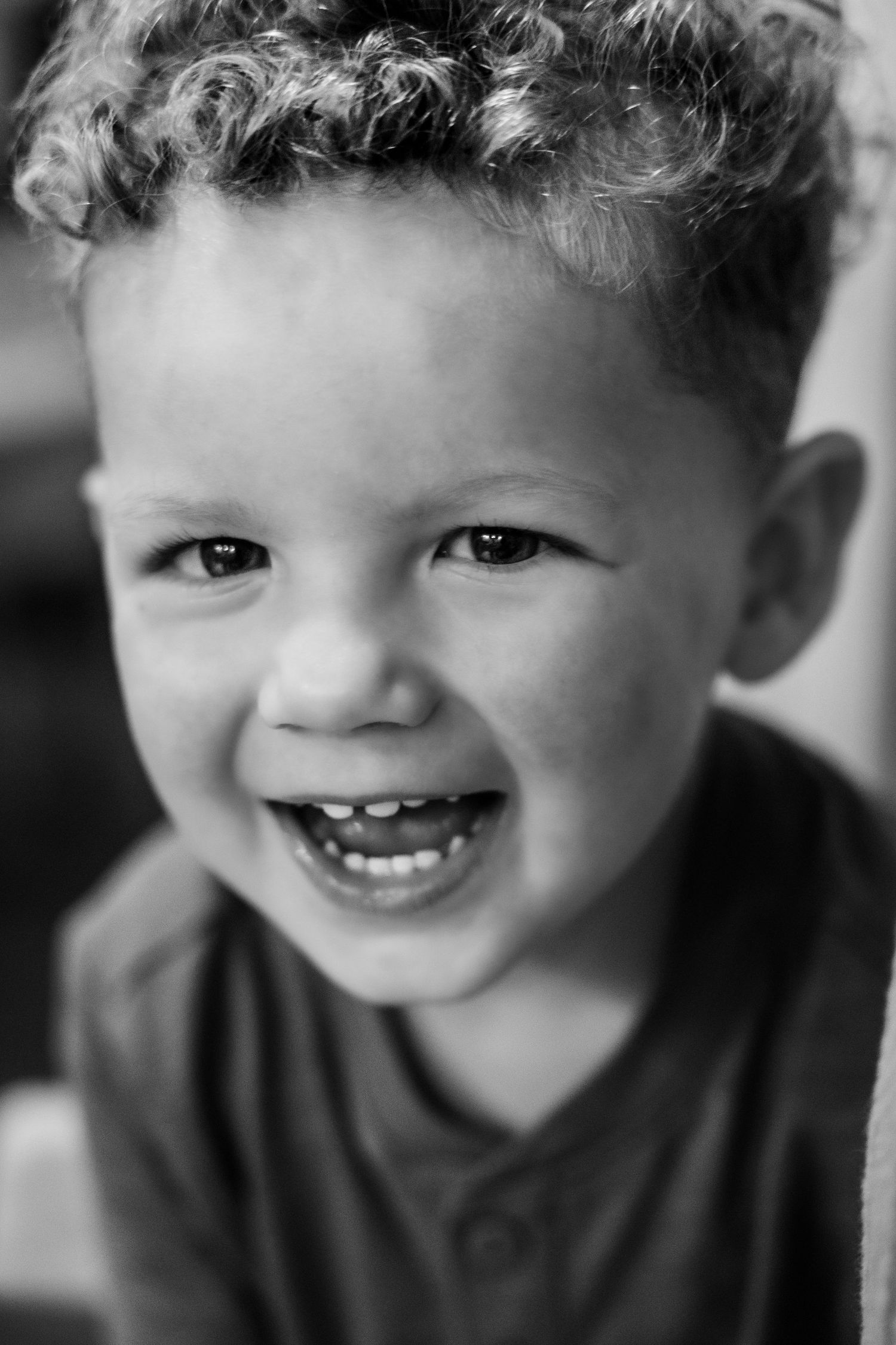 Black and white portrait of a happy toddler boy with curly hair laughing and showing his teeth.