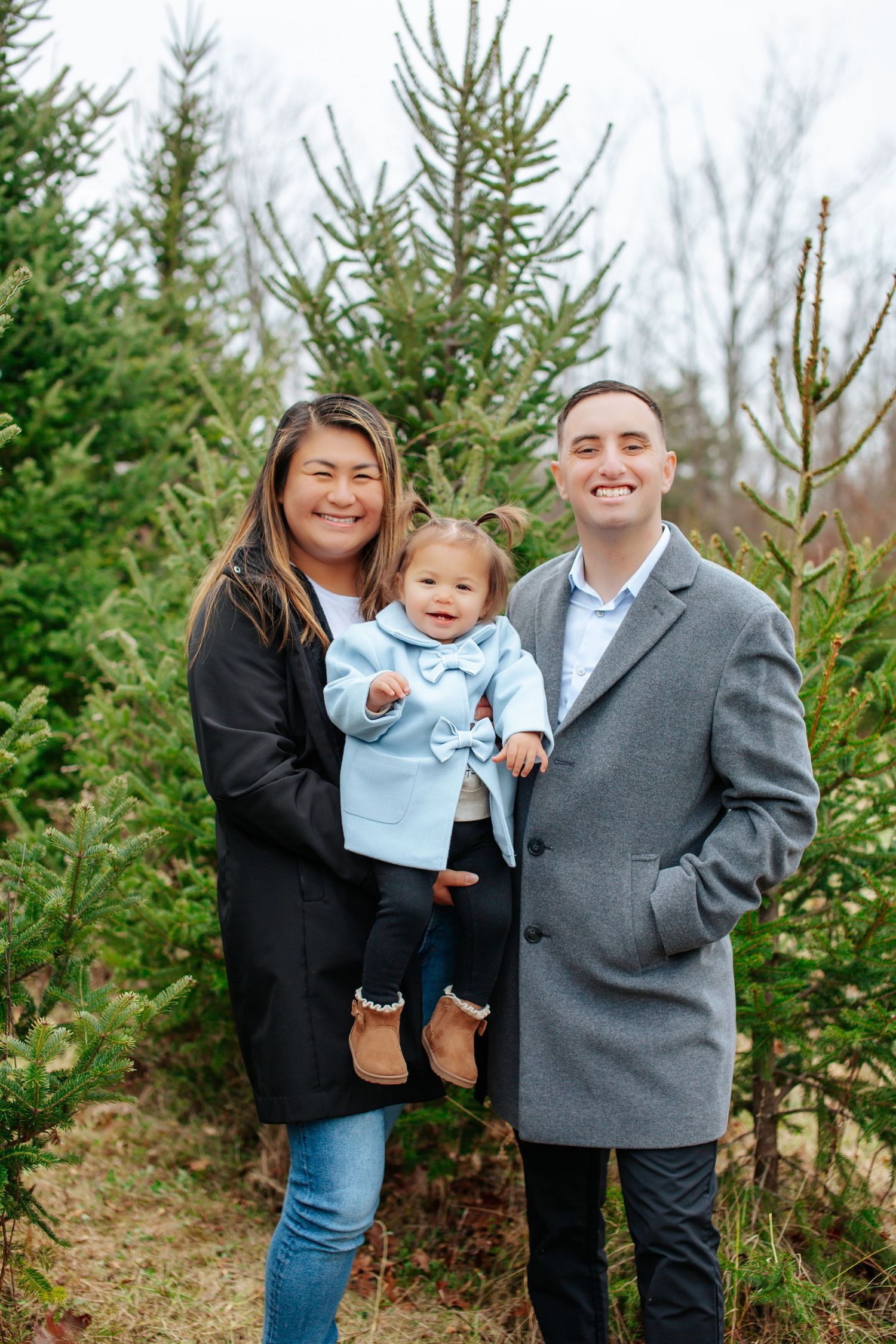 Family poses together among evergreen trees at Christmas tree farm during winter photoshoot.