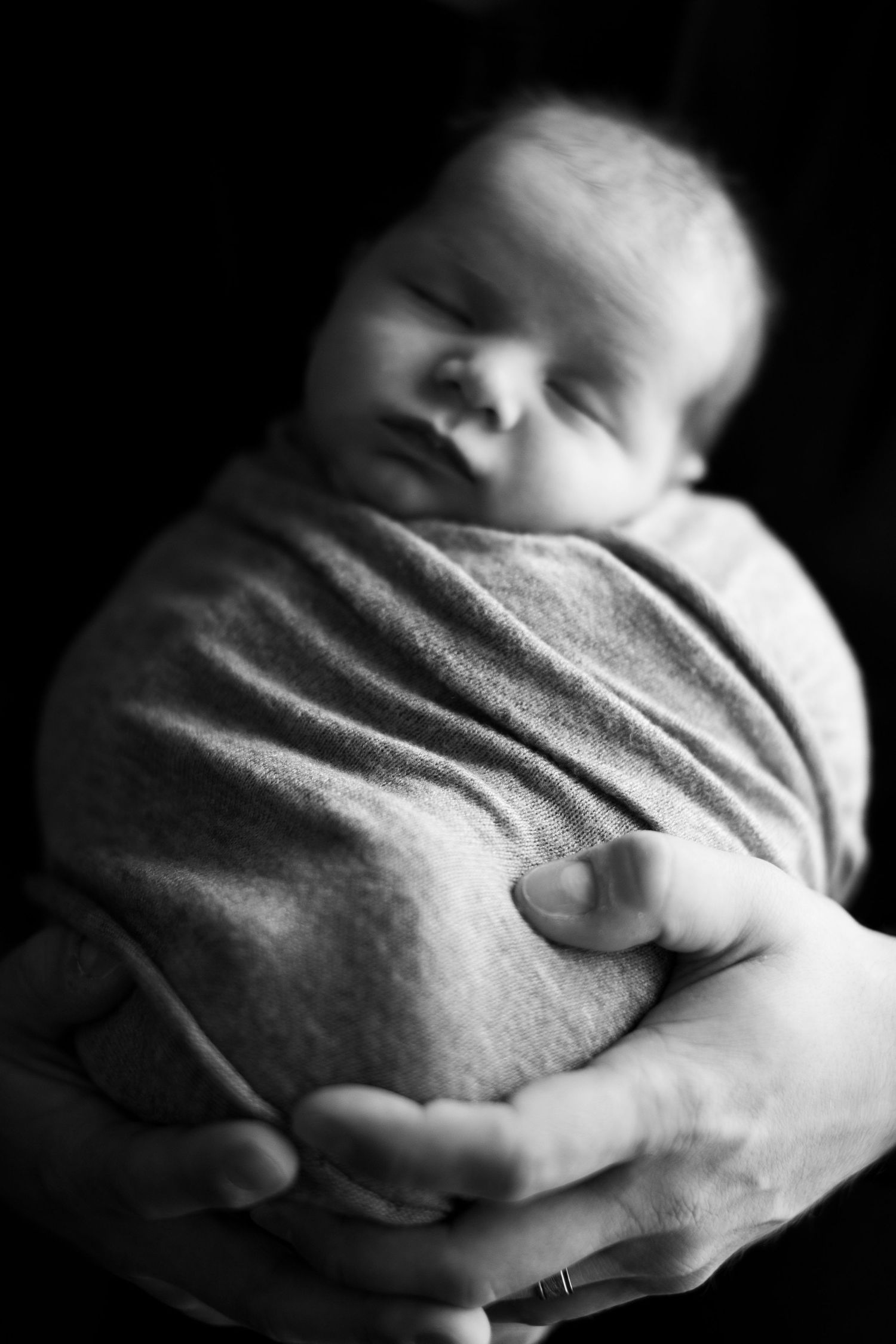 Black and white image of a sleeping newborn wrapped snugly in soft blanket.
