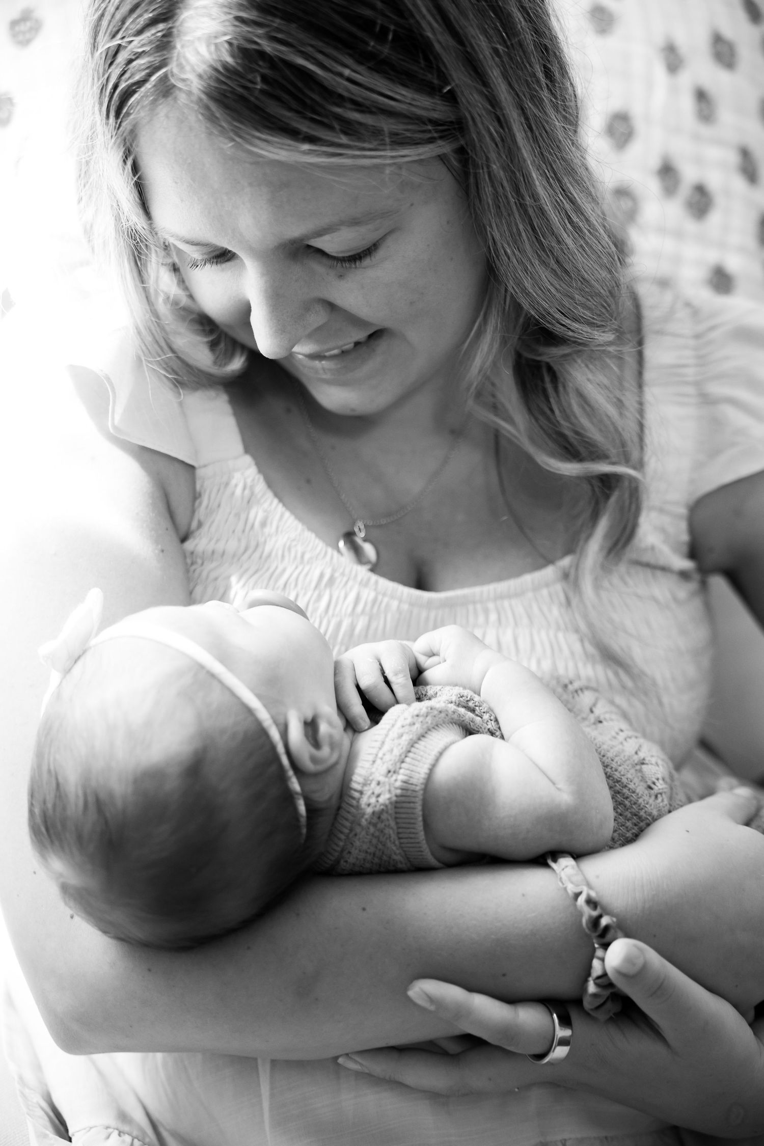 Black and white photo of a smiling mother tenderly cradling her newborn baby in her arms.