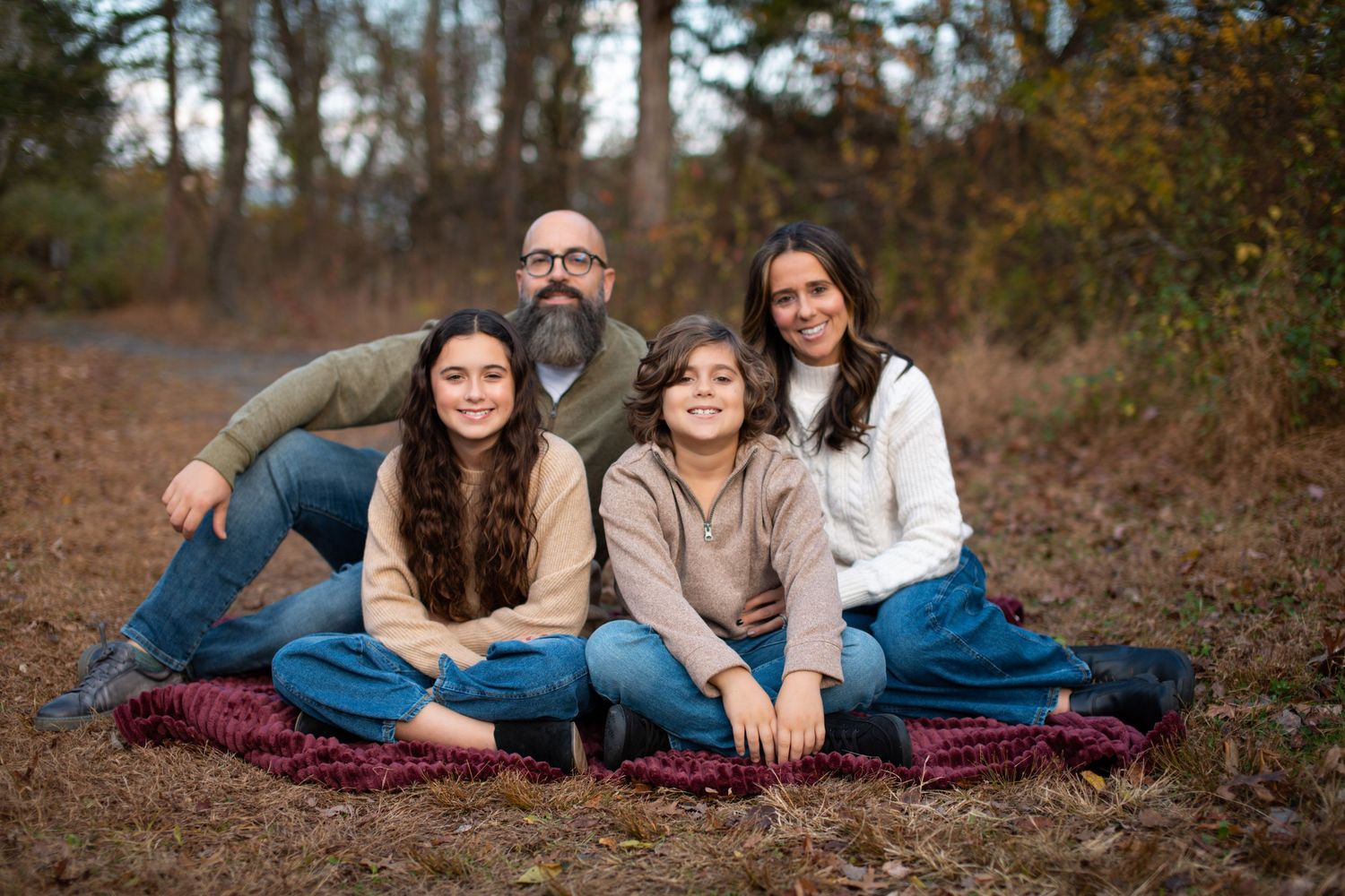 A casual family portrait on burgundy blanket with fall foliage in background.
