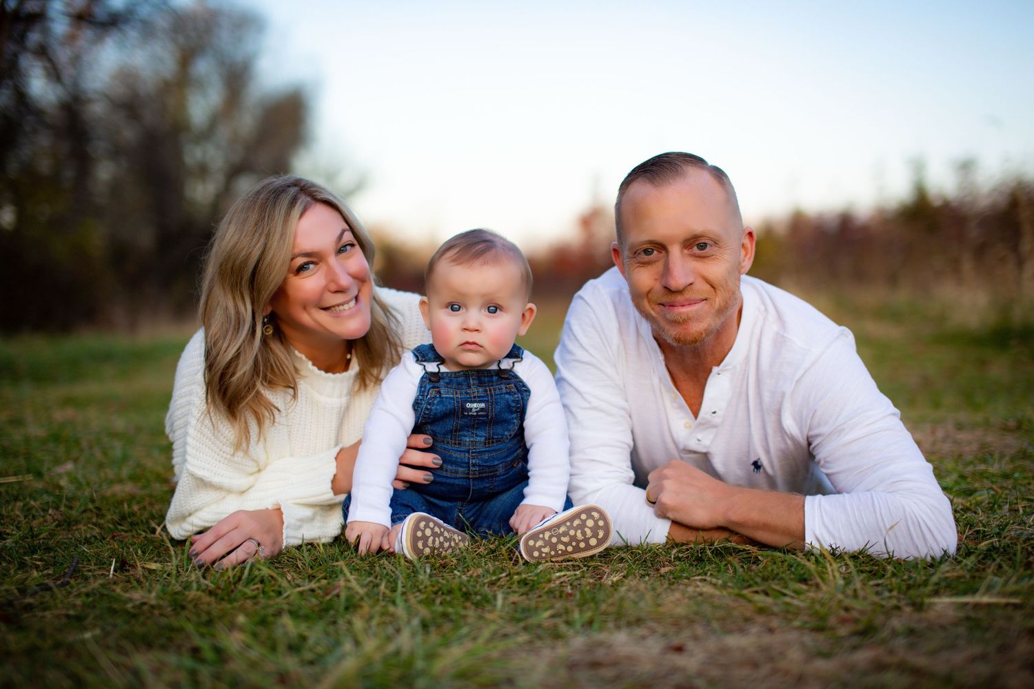 Family lying together on grass in outdoor portrait session during golden hour.