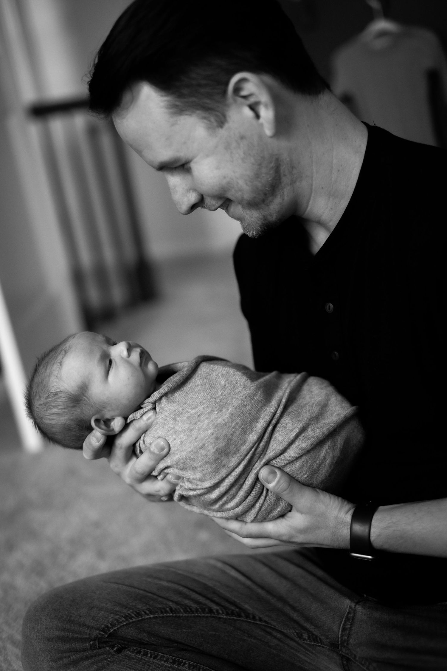 A tender black and white portrait of a parent holding a swaddled newborn baby in an intimate indoor setting.