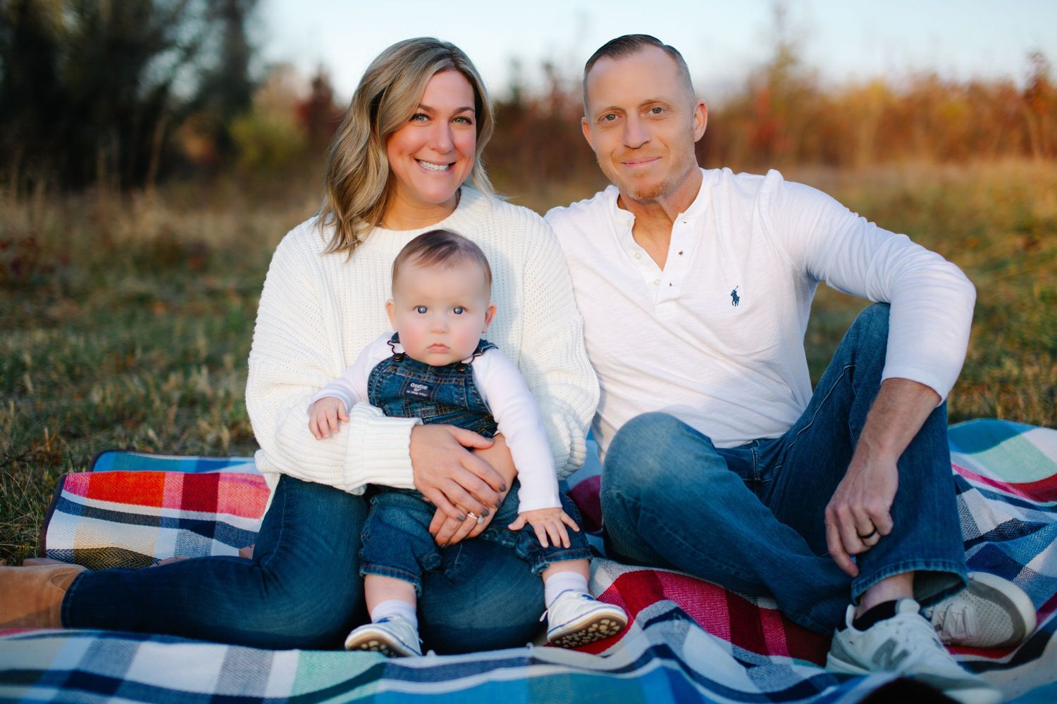 A family sits together on a blue blanket outdoors during a golden hour photoshoot in a natural setting.