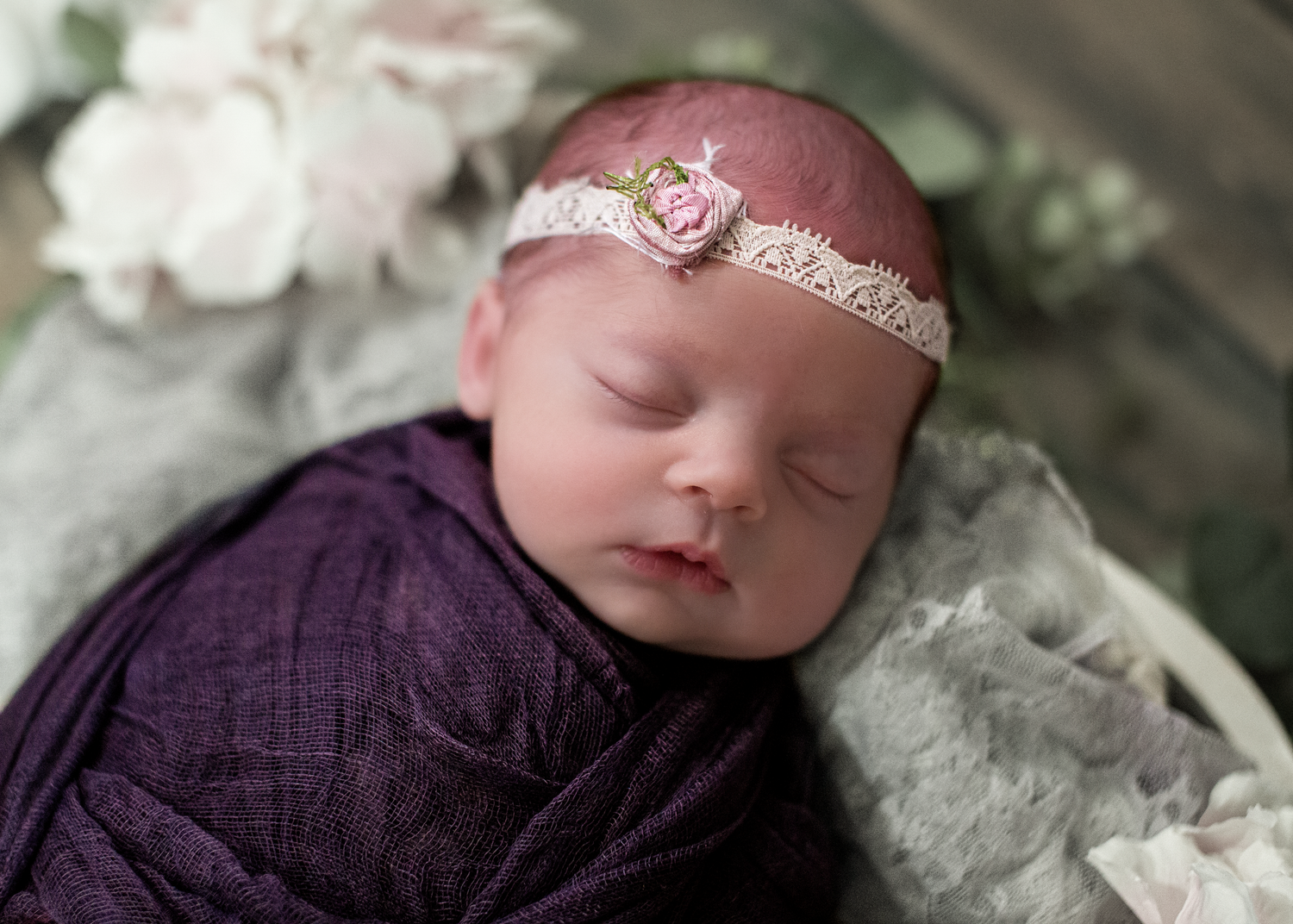 Newborn baby wrapped in purple fabric sleeping peacefully with delicate headband.
