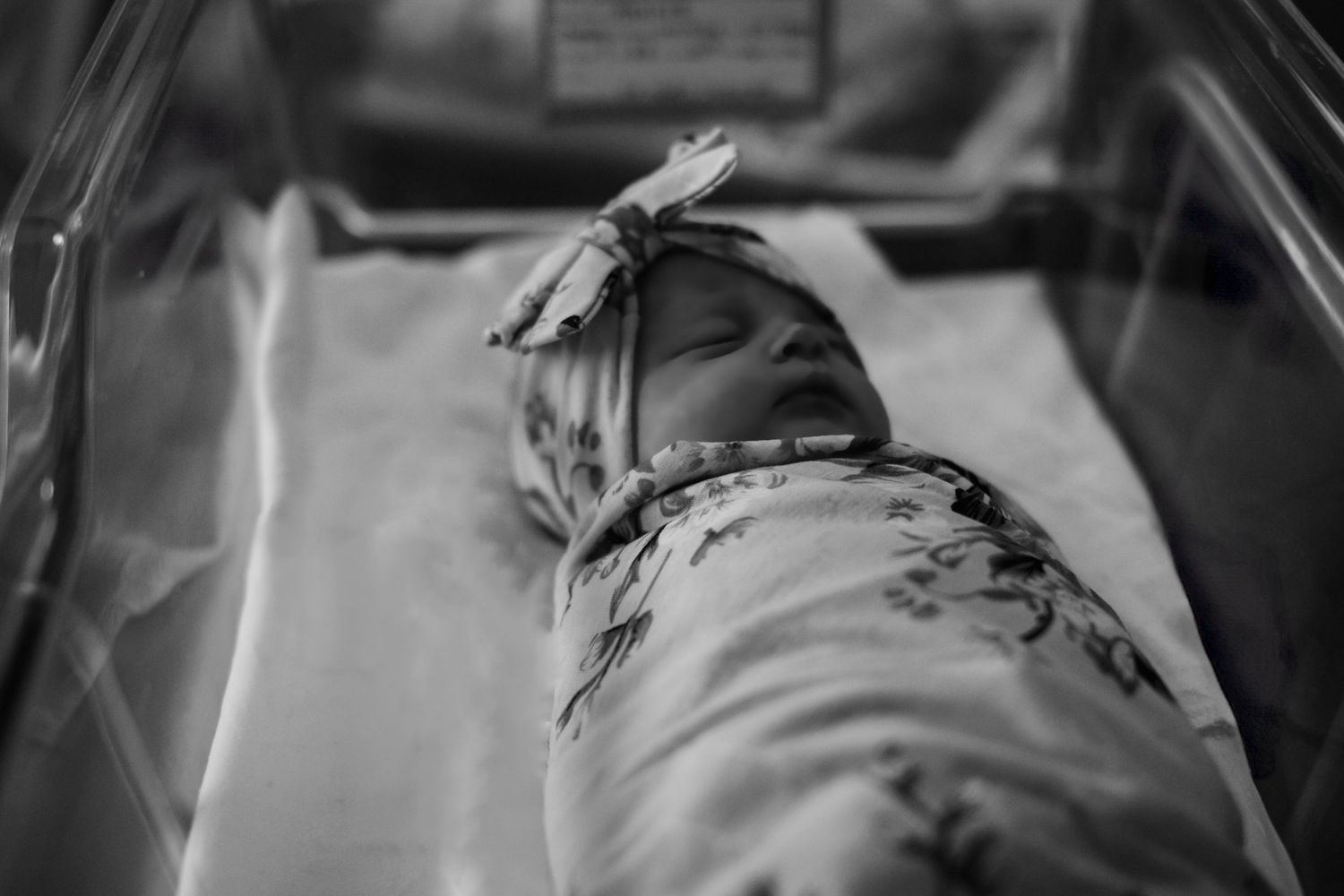 Newborn wrapped in a floral swaddle blanket sleeping peacefully on white bedding.