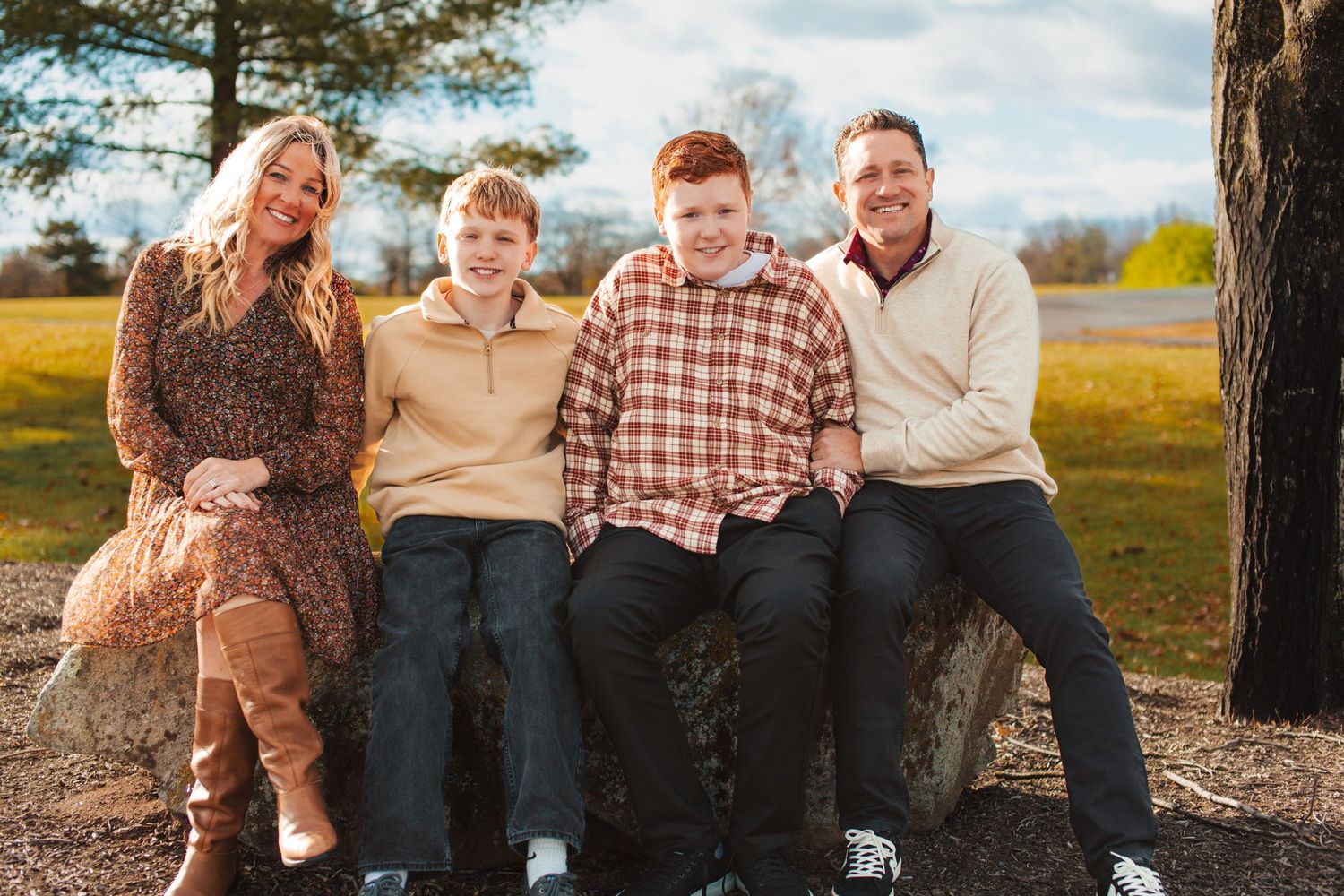 A happy family sits together outdoors on a sunny autumn day wearing coordinated casual outfits in earth tones.