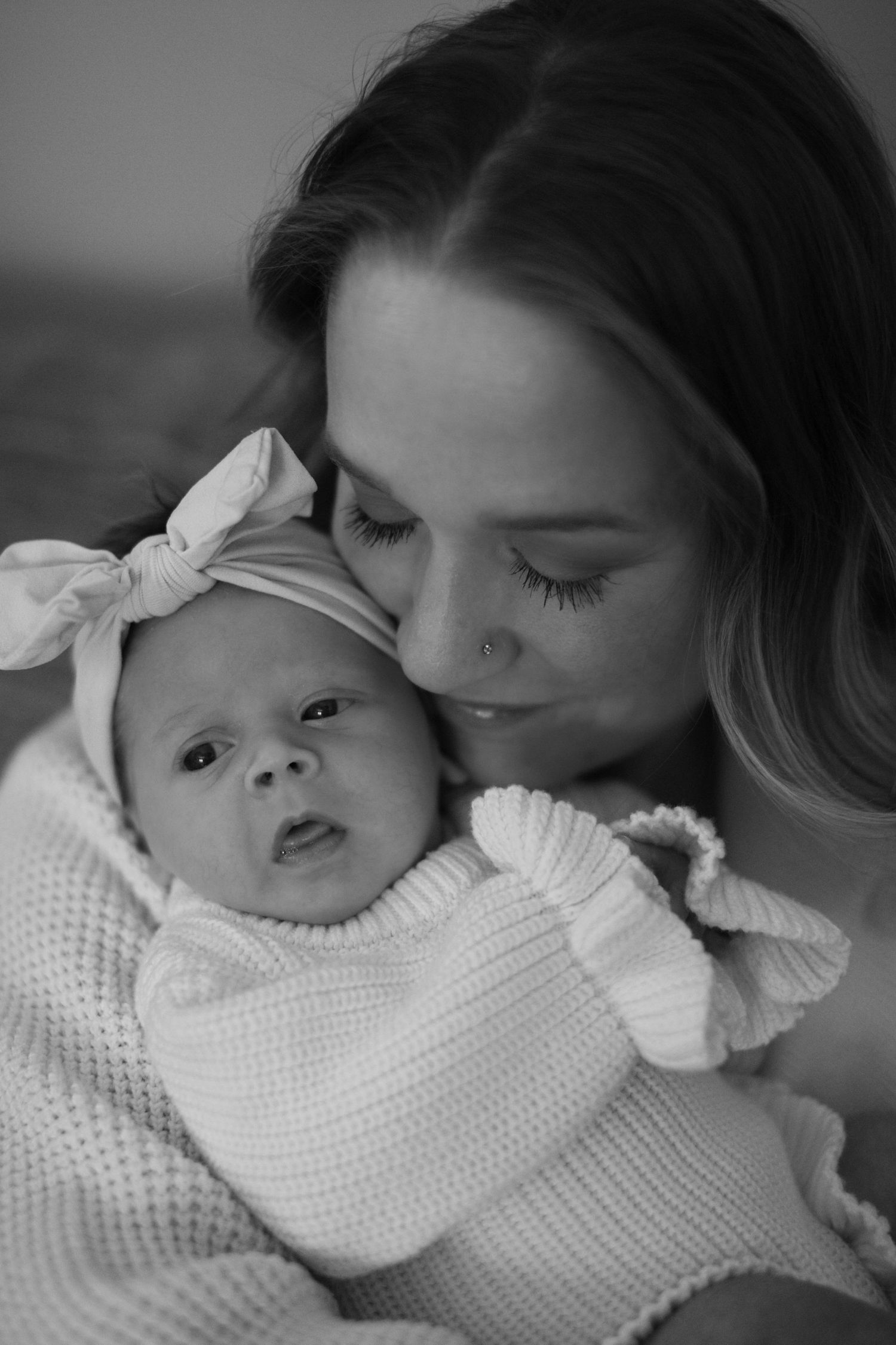 A tender black and white photo series showing a parent and baby sharing intimate moments while wearing white knit clothing.