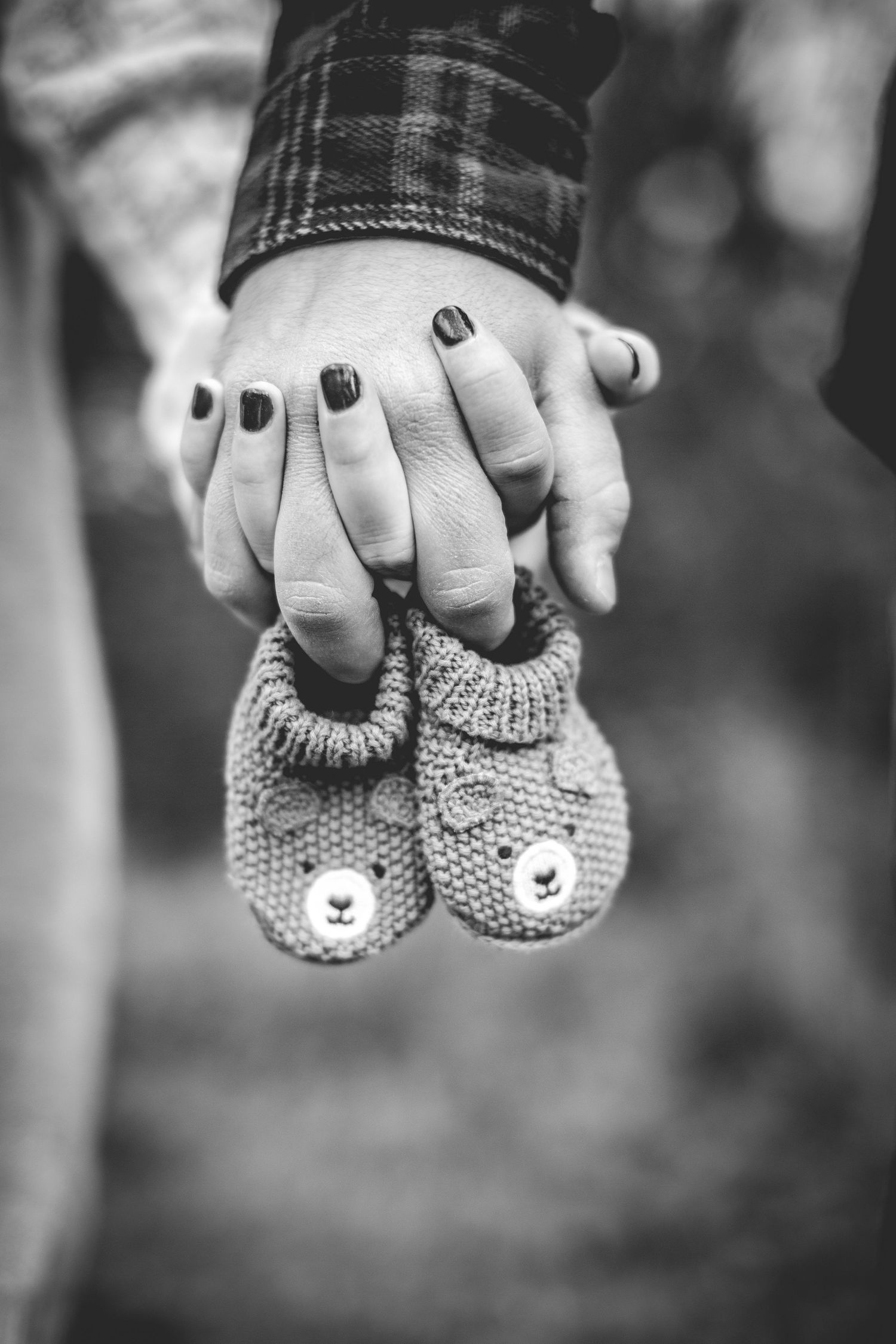 Black and white photo series showing hands holding tiny knitted baby booties in a pregnancy announcement style.