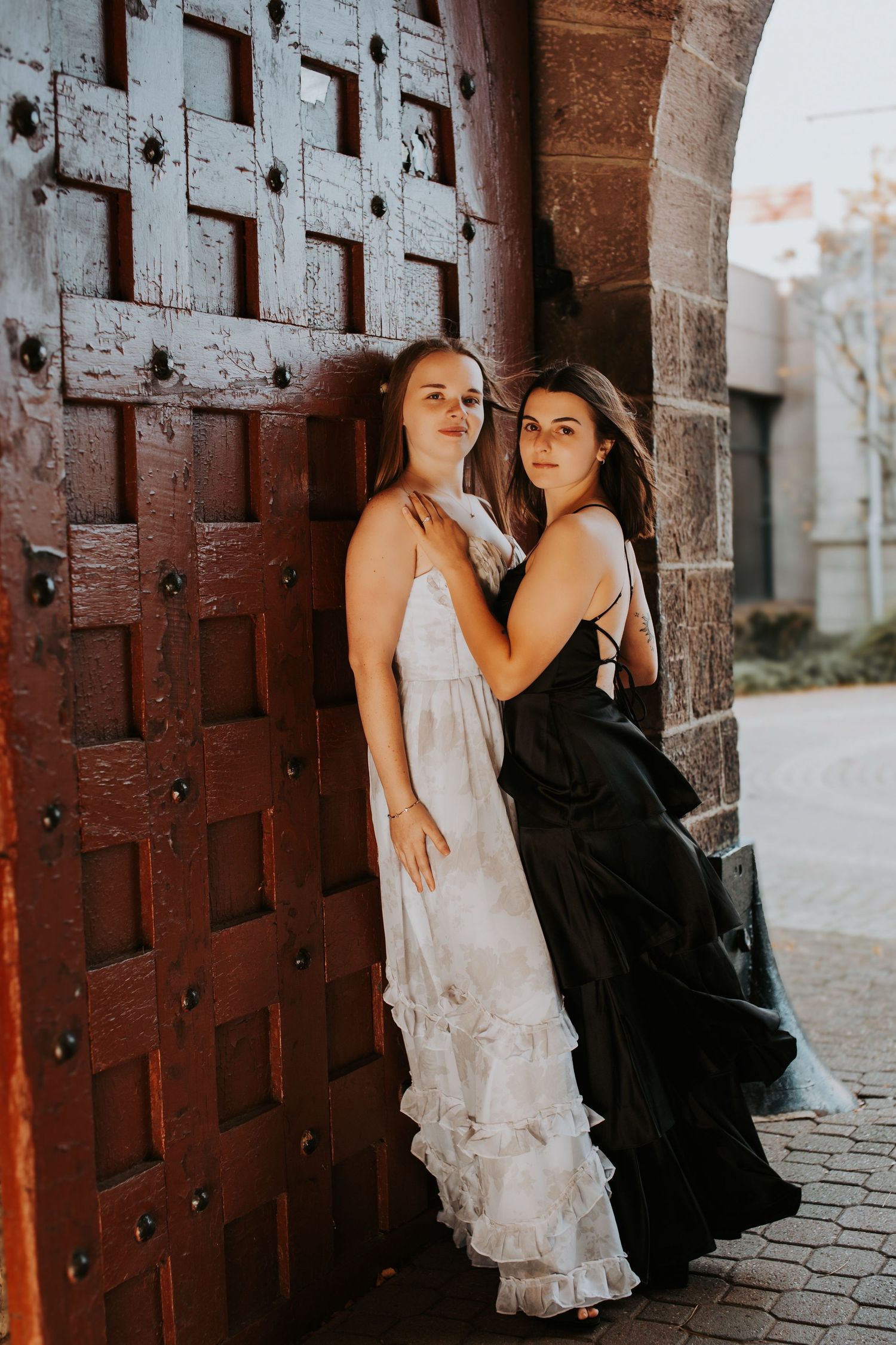 Two people in contrasting outfits pose intimately against a rustic wooden door backdrop.