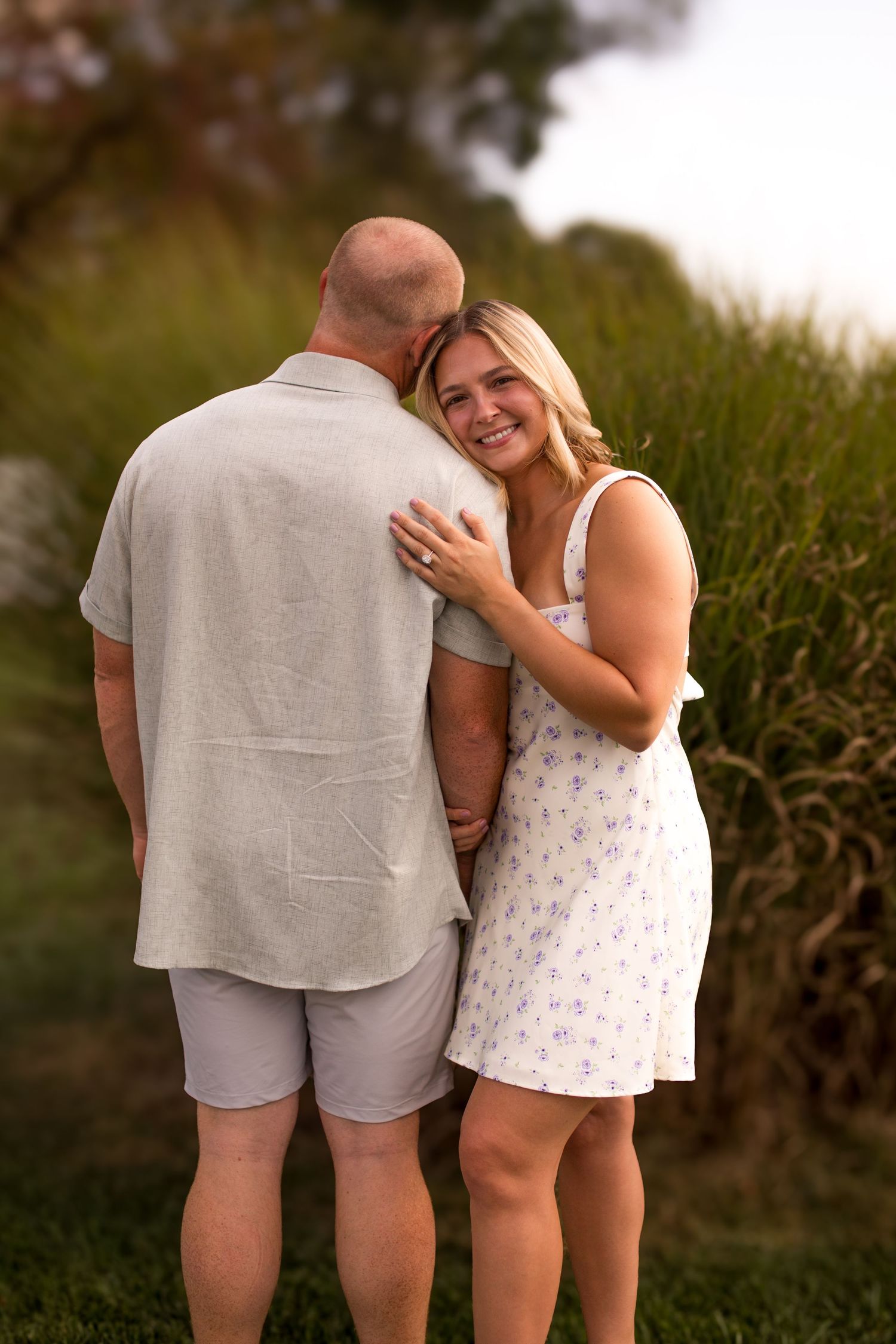 A couple shares intimate laughs together during an outdoor photoshoot in a grassy field at sunset.