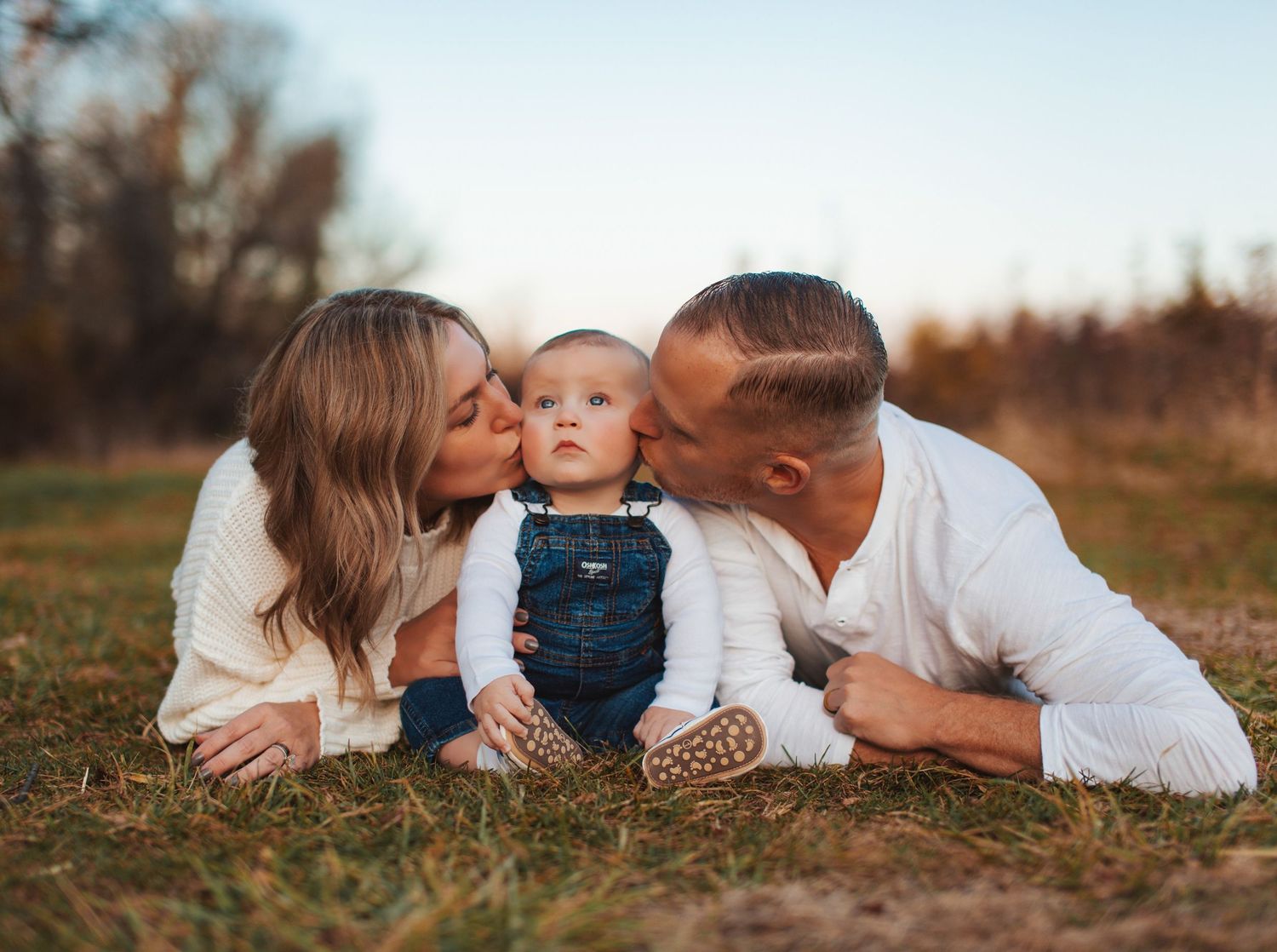 A family lies together on autumn grass during a warm sunset photoshoot.