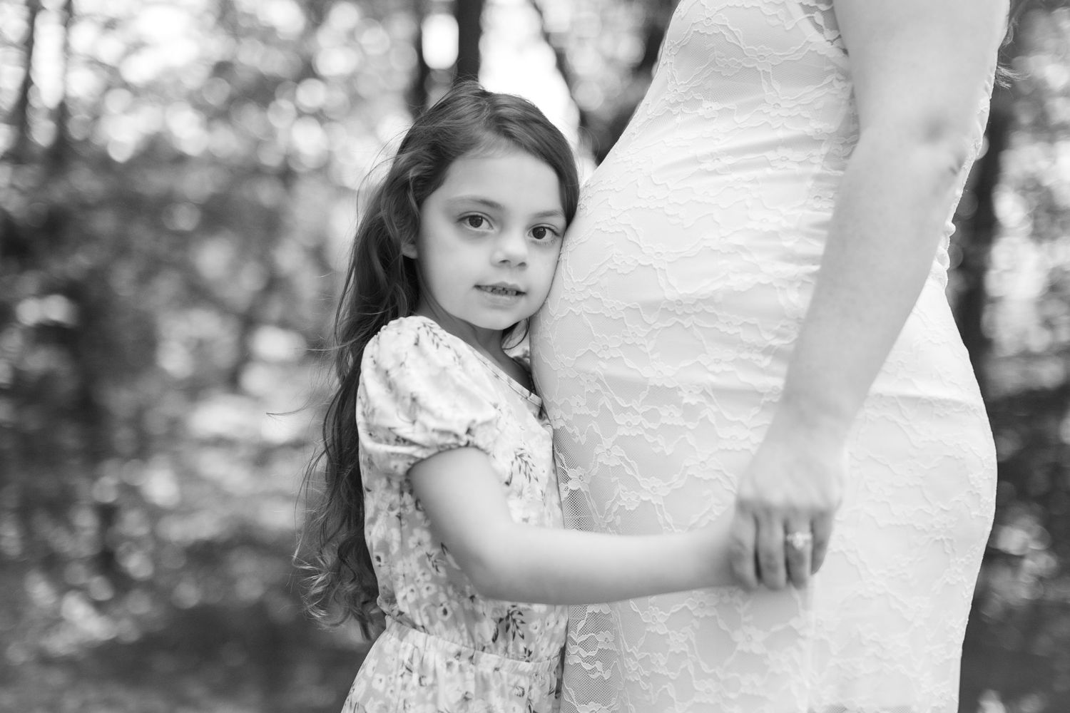 Intimate maternity portrait session in a white lace dress outdoors.